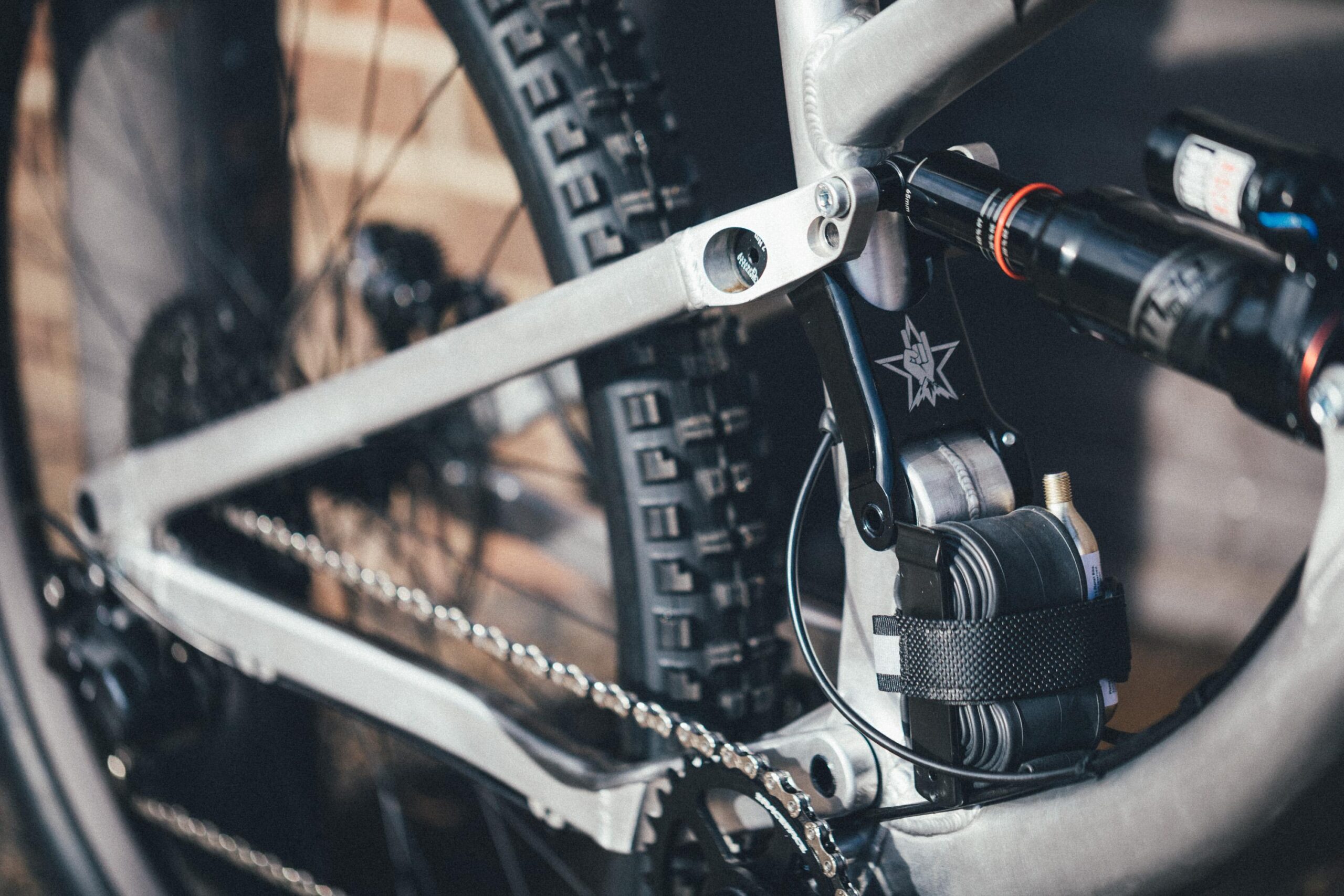 Guerrilla Gravity Megatrail: Close-up image of a mountain bike frame, showcasing the rear suspension system, chain, and tire. The metallic finish of the frame contrasts with the black components, emphasizing the intricate mechanical details.