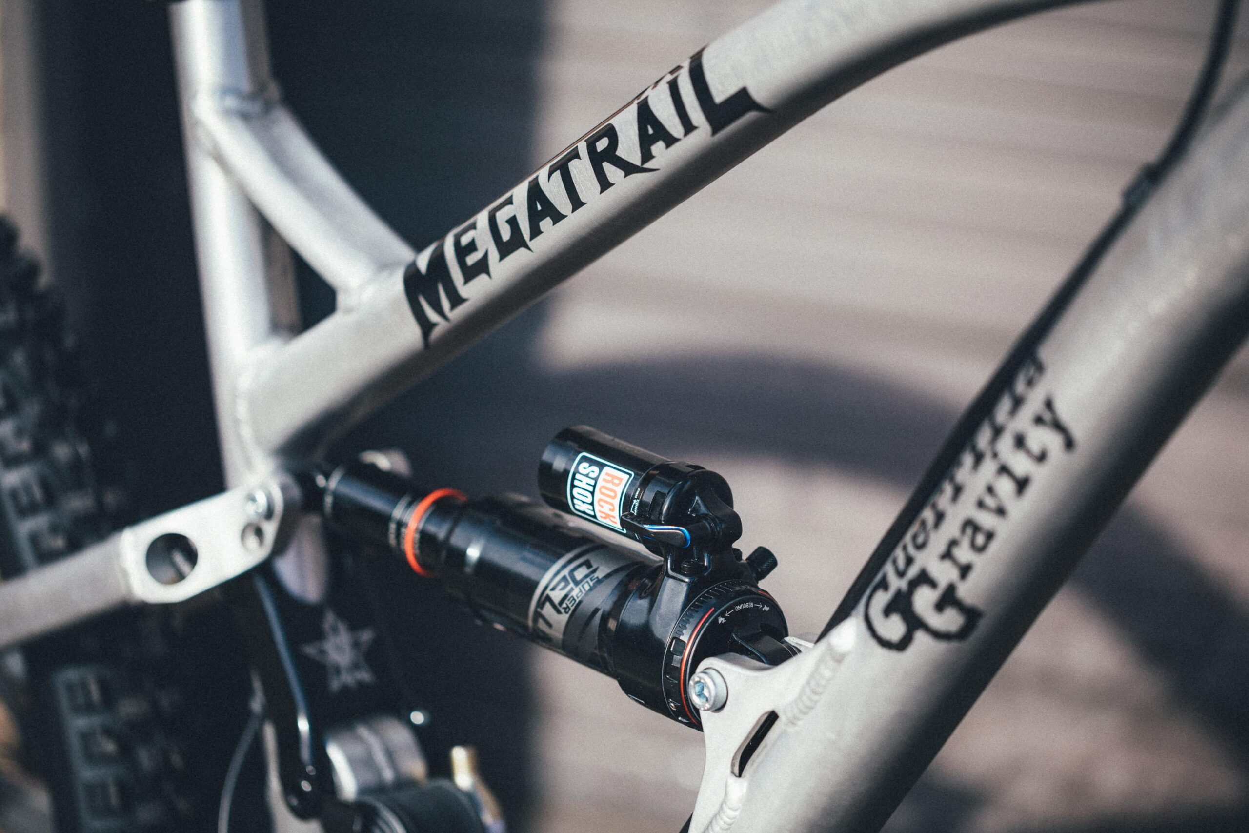 Guerrilla Gravity Megatrail: Close-up of a mountain bike frame with "MEGATRAIL" branding, featuring a black shock absorber labeled "ROCKSHOX" and detailed components, highlighting the bike's suspension setup.