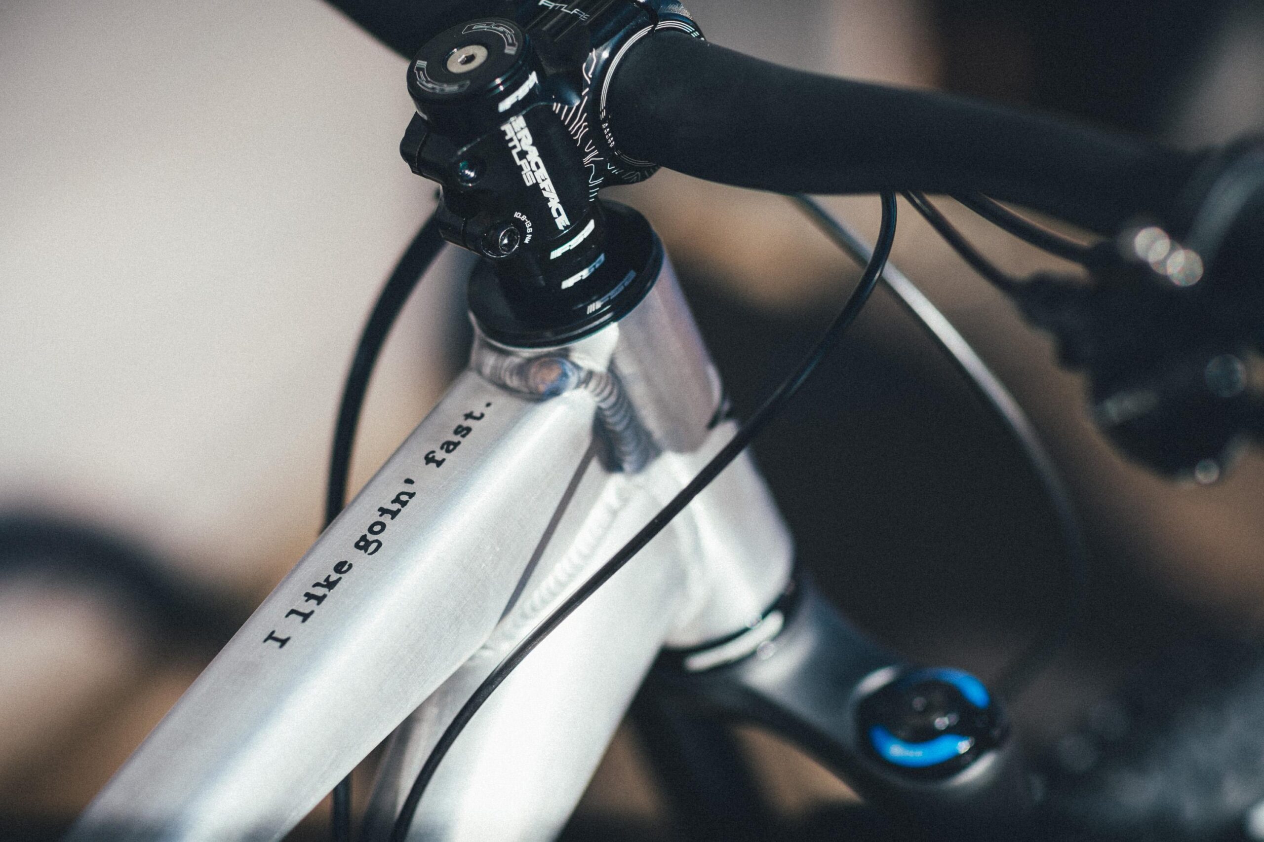 Guerrilla Gravity Megatrail: Close-up of a bicycle's handlebars and frame, featuring the inscription "I like goin' fast." The frame appears metallic with a smooth finish, and the components include a black stem and handlebar.