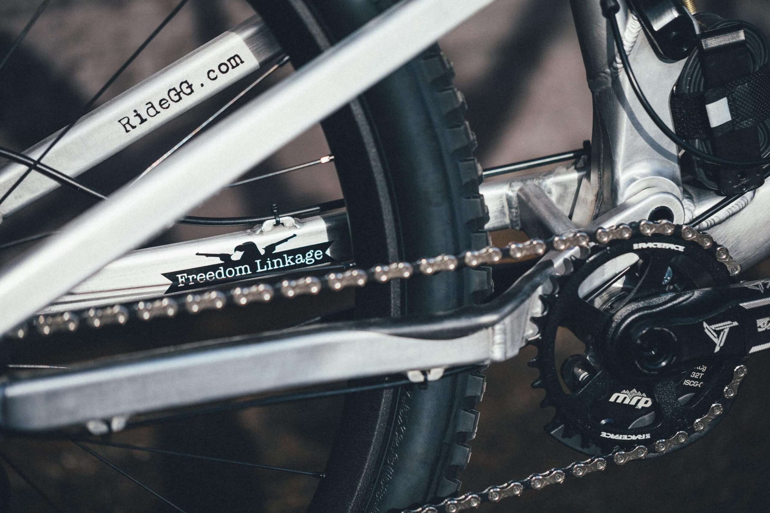 Guerrilla Gravity Megatrail: Close-up view of a bicycle's drive train, showcasing the chain, pedals, and a portion of the frame. The frame features the text "RideGG.com" and "Freedom Linkage," along with a black logo silhouette. The image highlights the mechanical details and design of the bike.