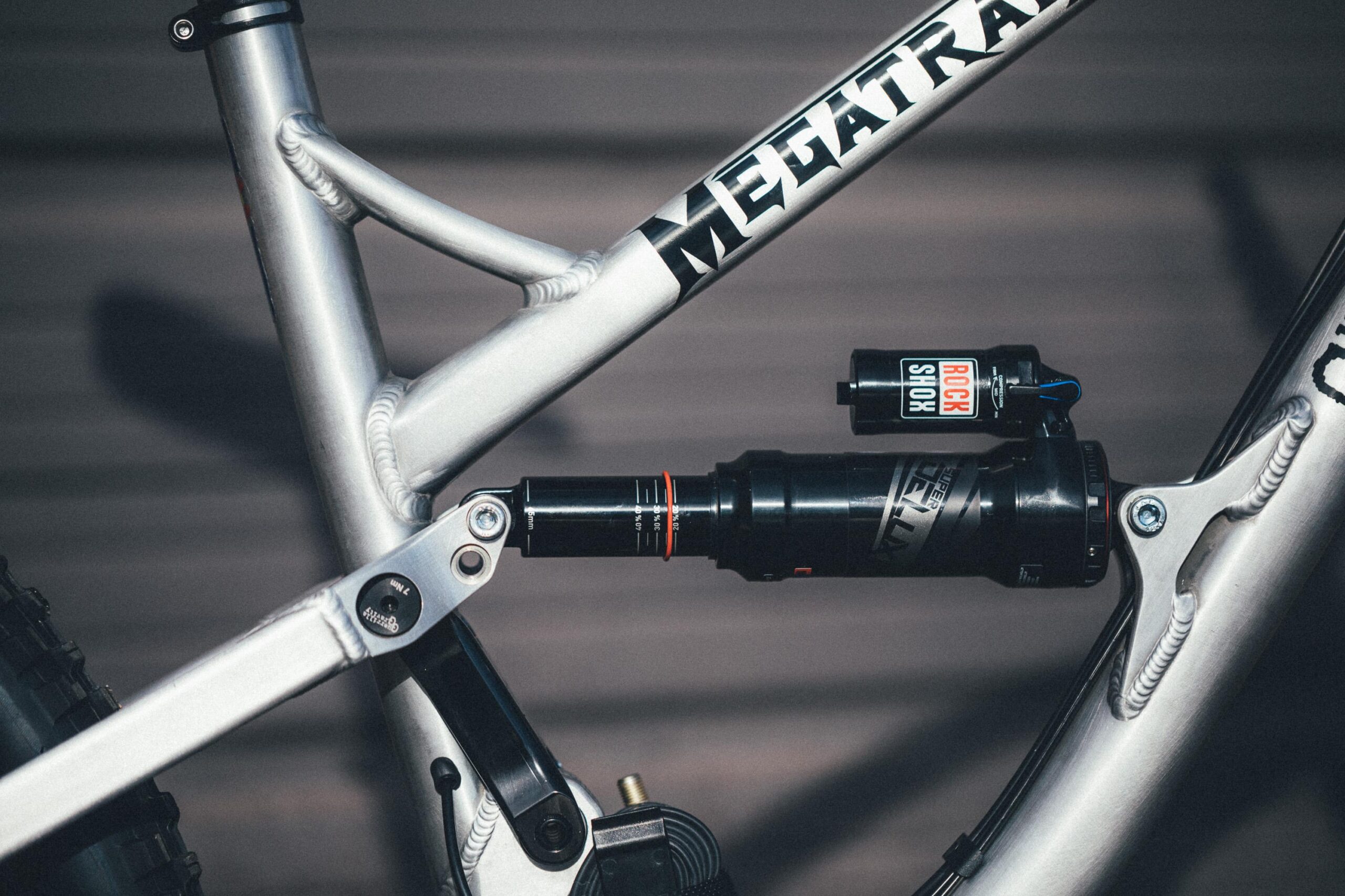 Guerrilla Gravity Megatrail: Close-up of a mountain bike frame, showcasing the suspension components including a RockShox shock absorber. The frame is silver with a prominent logo. The image highlights the bike's mechanical details and design.