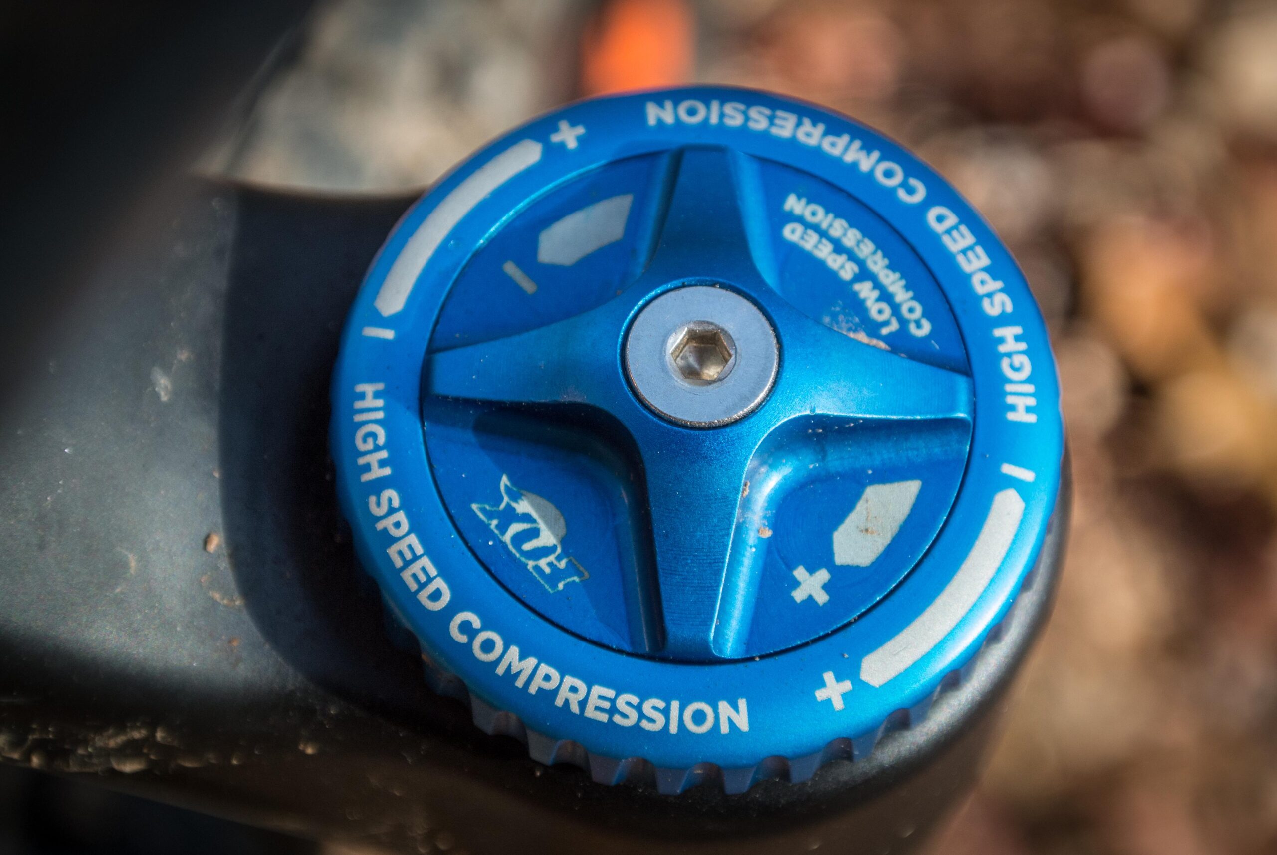 Orange Five RS: Close-up view of a blue knob labeled "High Speed Compression," used for adjusting suspension settings on a bicycle or similar equipment, with markings indicating a range for adjustments. The background features blurred natural elements.