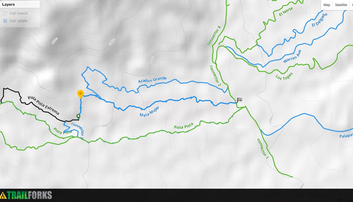 A map showing various mountain biking trails with blue, green, and black routes labeled with names like "Pista Pista," "Mala Mujer," and "Azadon Grande." Elevation lines are depicted in shades of gray, and the map includes markers for trail heads. Mala Mujer mountain bike trail.