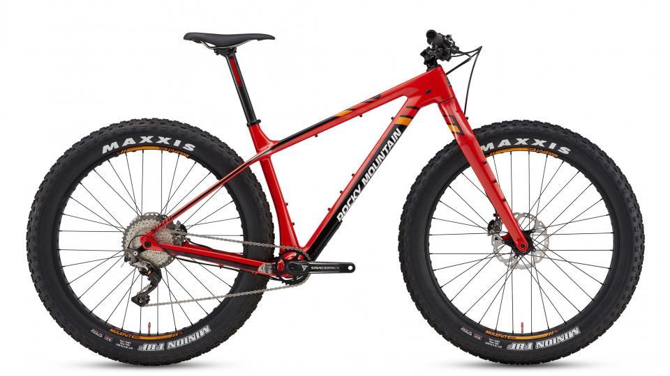 Rocky Mountain Suzi Q: A red and black mountain bike with thick tires, featuring a sleek frame, disc brakes, and a gear system. The bike is positioned on a white background, showcasing its design and components, including Maxxis tires and a Rocky Mountain branding.