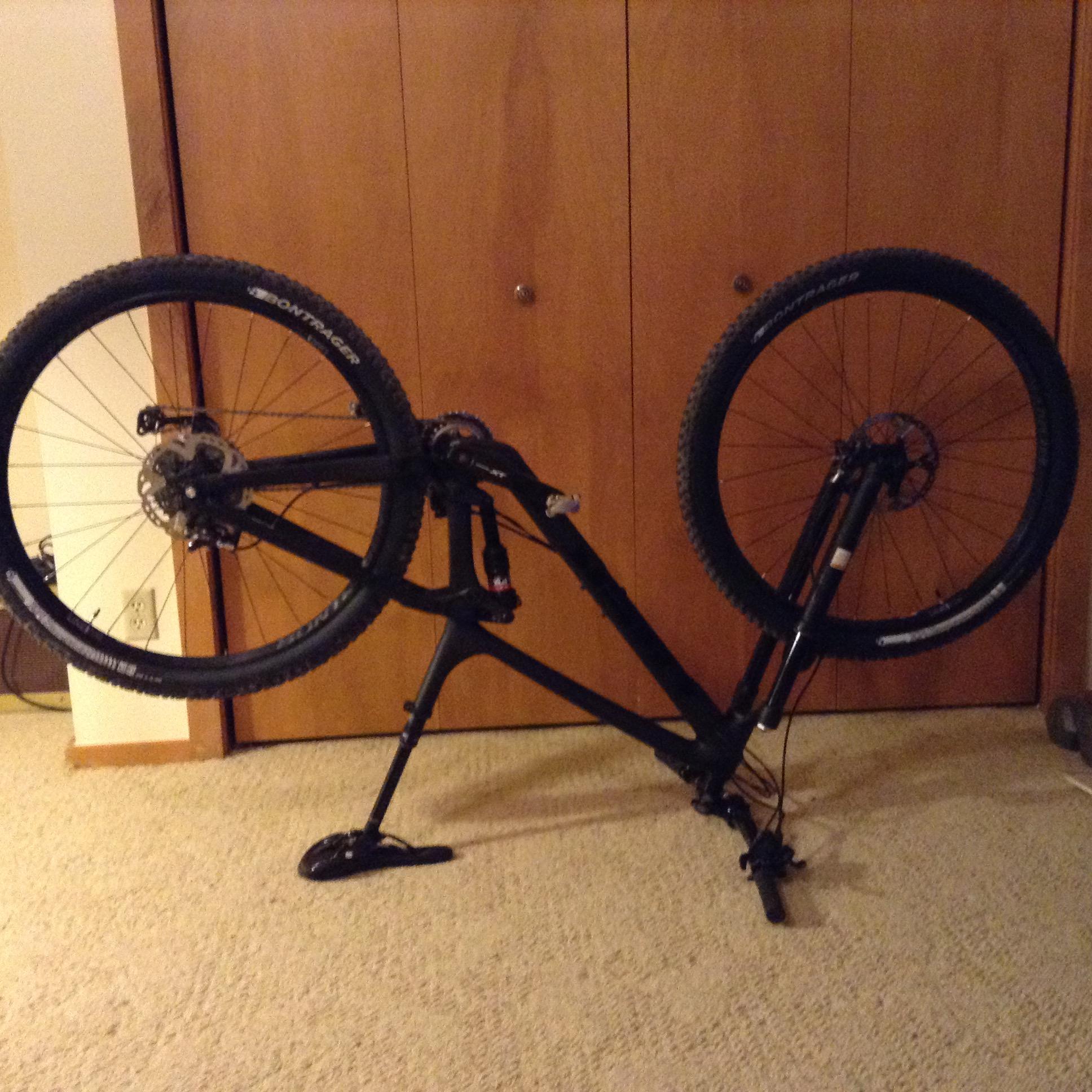 Trek Fuel EX 9.8: Image of a black mountain bike turned upside down, resting on its handlebars and rear wheels. The background shows simple wooden cabinetry. The floor is covered with light-colored carpet.