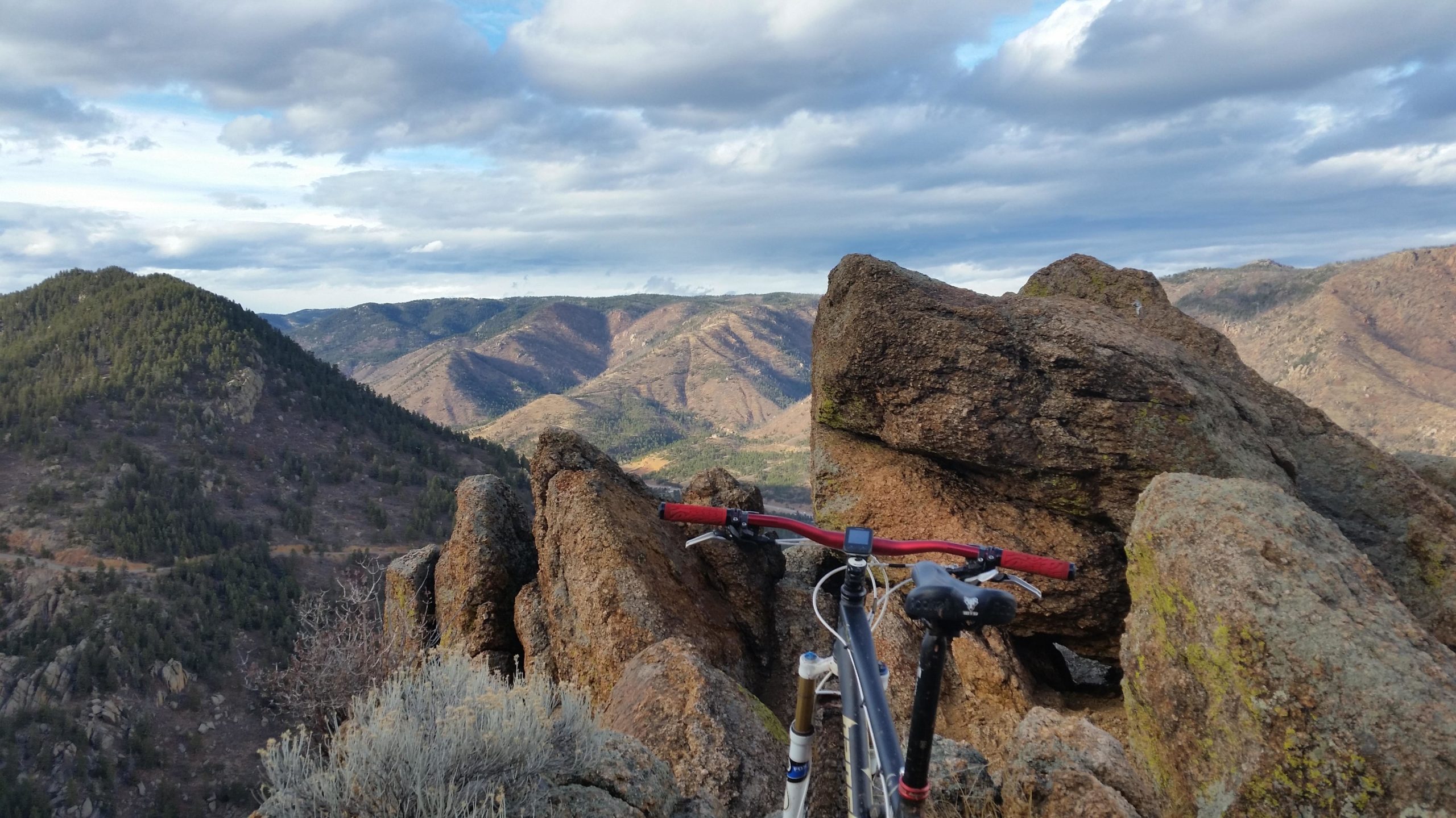 A mountain bike resting on rocks with a scenic view of rolling hills and valleys under a cloudy sky. Heizer Trail mountain bike trail.