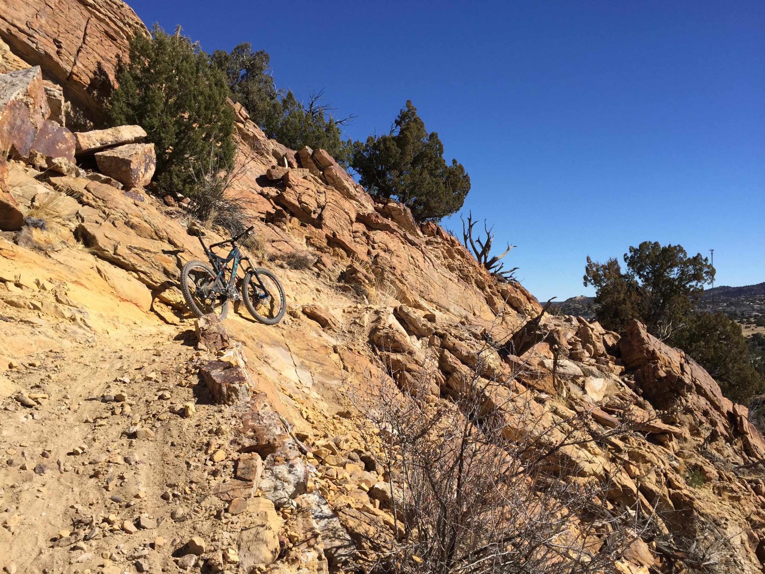 Mountain bike resting on a rocky trail, surrounded by rugged terrain and sparse vegetation under a clear blue sky. South Canon Trails mountain bike trail.