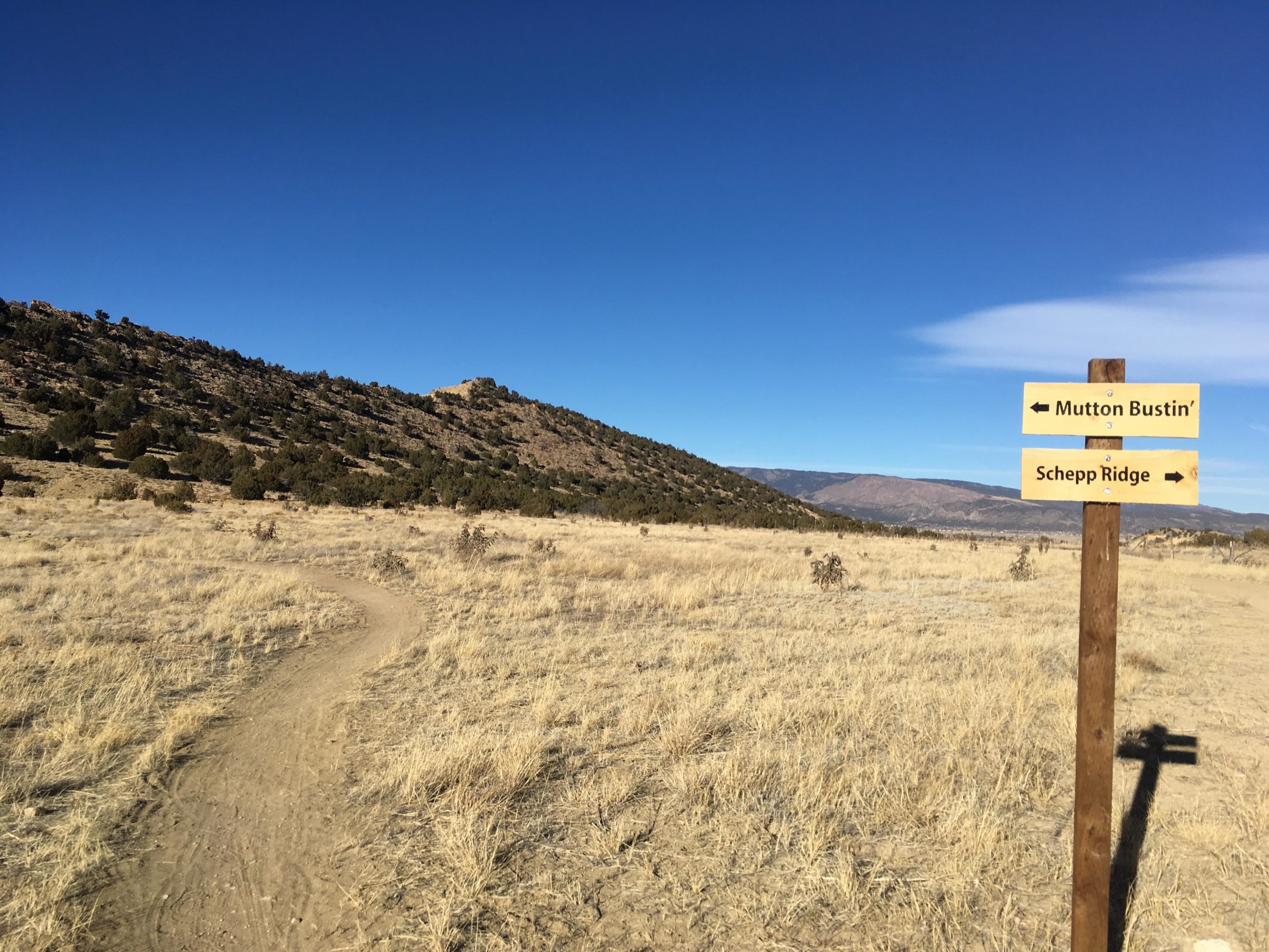 A scenic outdoor trailmarked by a wooden signpost showing directions to "Mutton Bustin
