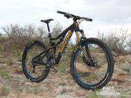 Santa Cruz Bronson: A black and orange mountain bike positioned on rocky terrain, surrounded by sparse vegetation under an overcast sky.