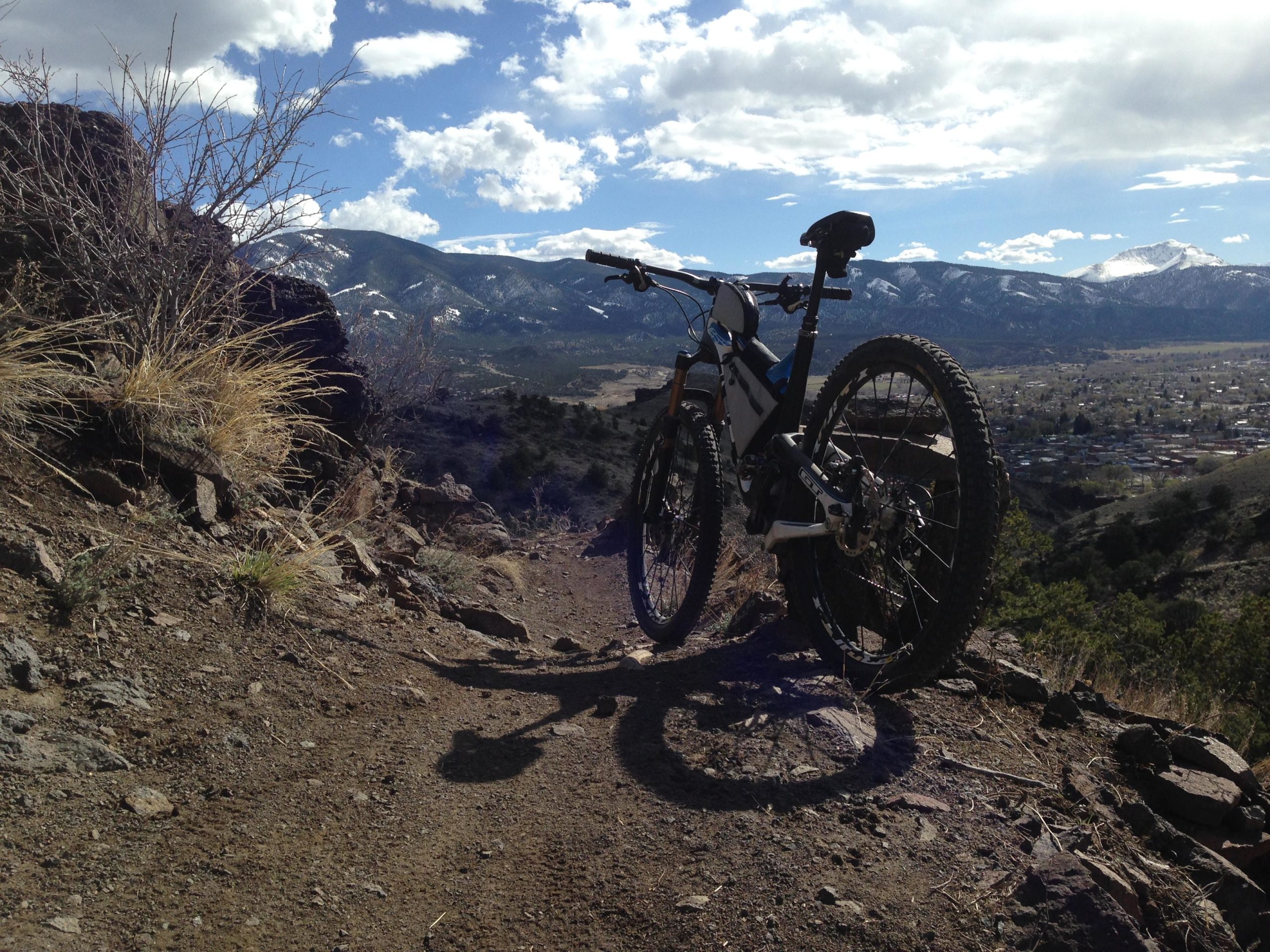 A mountain bike parked on a dirt trail with a scenic view of mountains and a valley in the background, featuring a partly cloudy sky. Arkansas Hills mountain bike trail.