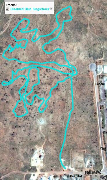 A satellite image showing a trail map with winding paths designated in bright blue over a barren landscape. Nearby structures include a hospital, a school, and a road labeled "Fallon Rd." The area appears primarily unoccupied with minimal vegetation. Disabled Blue mountain bike trail.