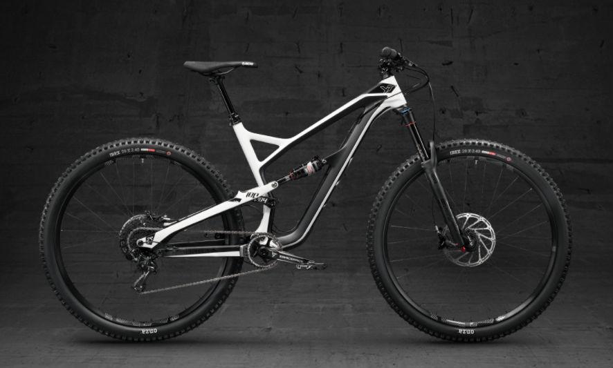 Yt industries Jeffsy: A sleek, modern mountain bike with a white and black frame design, featuring wide, knobby tires and a front suspension fork. The bike is positioned against a dark, textured backdrop, highlighting its sporty features and high-performance components.