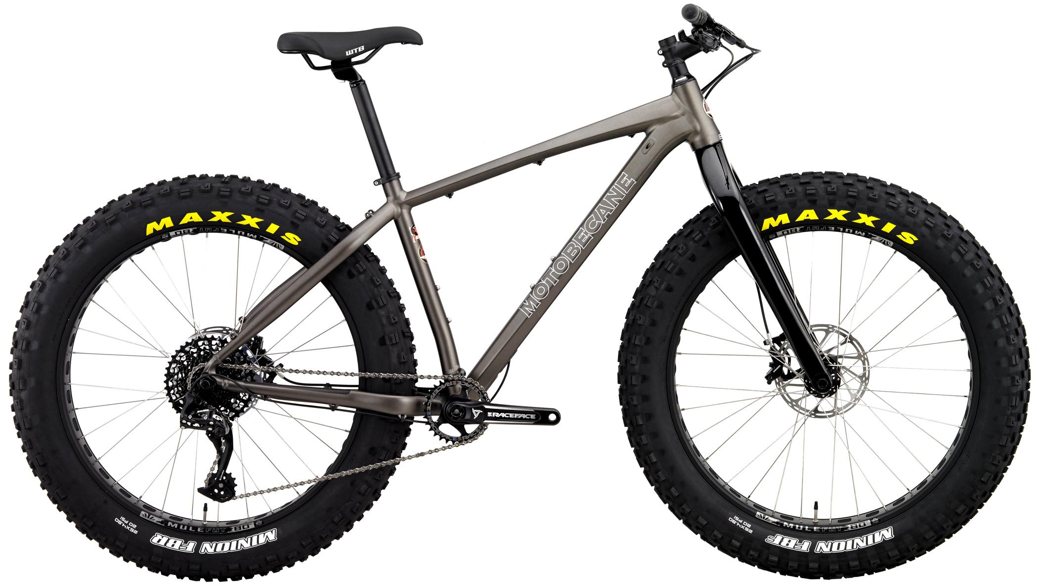 Motobecane NightTrain Express: A sturdy fat bike with a metallic gray frame and large, knobby tires designed for off-road cycling. The bike features a WTB saddle, a black fork, and Shimano components, highlighting its robust design for rough terrain. The tires are labeled with "Maxxis" and "Minion FBF," indicating high-performance capabilities.