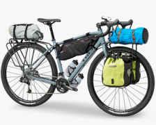 Trek Trek 920: A touring bicycle equipped with various bags and gear, including a gray bag on the front, a blue rolled-up bag, and two side panniers, one in bright yellow. The bike is positioned on a white background.