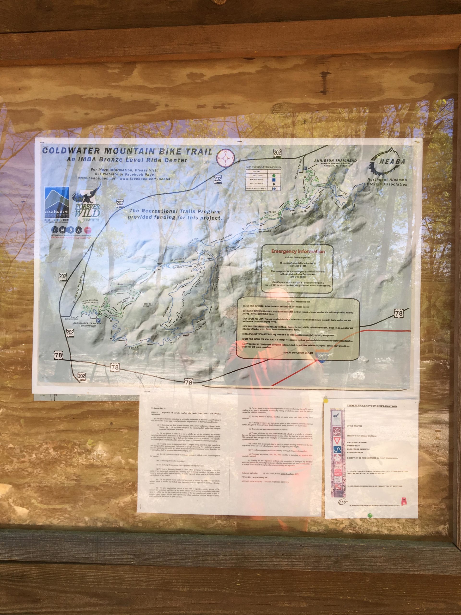 Map of the Coldwater Mountain Bike Trail, detailing routes and safety information, displayed on a wooden board. The map includes information about the trail's designation as an IMBA Bronze Level Ride Center, emergency contact details, and a list of recommended trail usage guidelines. Coldwater Mountain mountain bike trail.