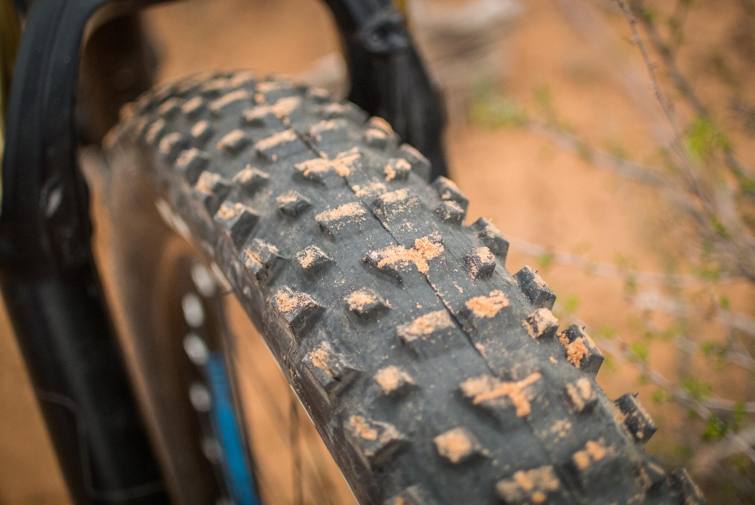 Rocky Mountain Pipeline: Close-up of a mountain bike tire with a textured, knobby surface covered in a light layer of dirt, sitting against a blurred, sandy background.