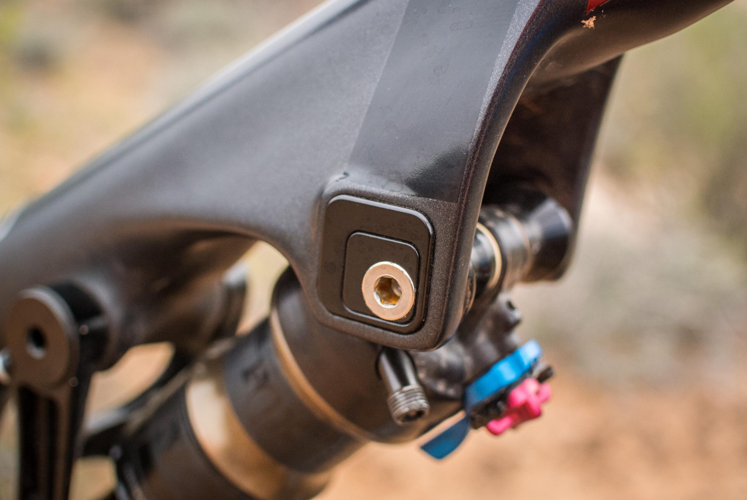 Rocky Mountain Pipeline: Close-up image of a mountain bike suspension component, showcasing a black frame part with a square mounting area and a threaded insert, alongside a suspension mechanism featuring colorful adjustment knobs. The background is blurred, indicating an outdoor setting.