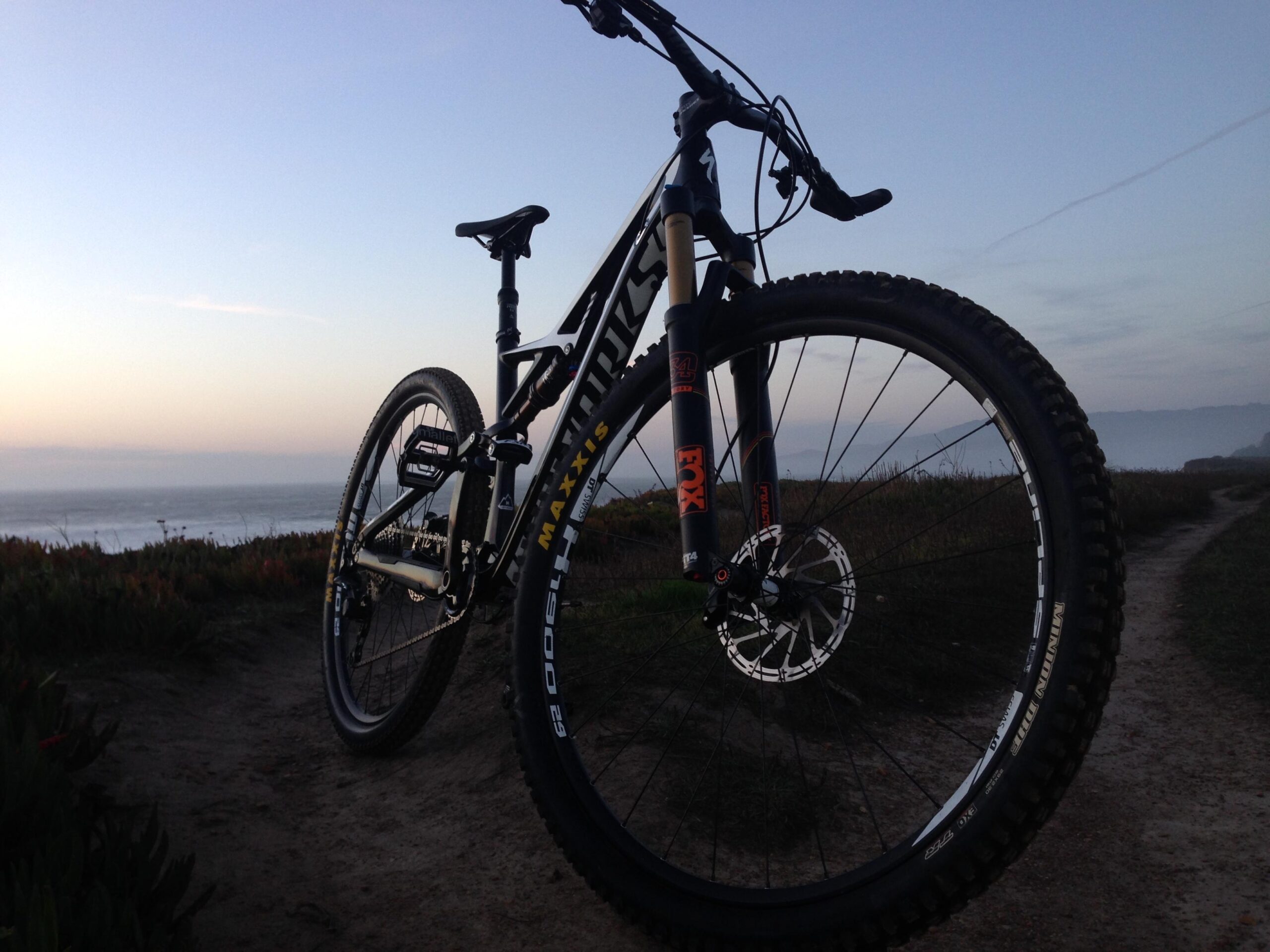 Specialized S-Works Camber 29: A close-up view of a mountain bike positioned on a scenic path, with the ocean in the background. The image captures the bike