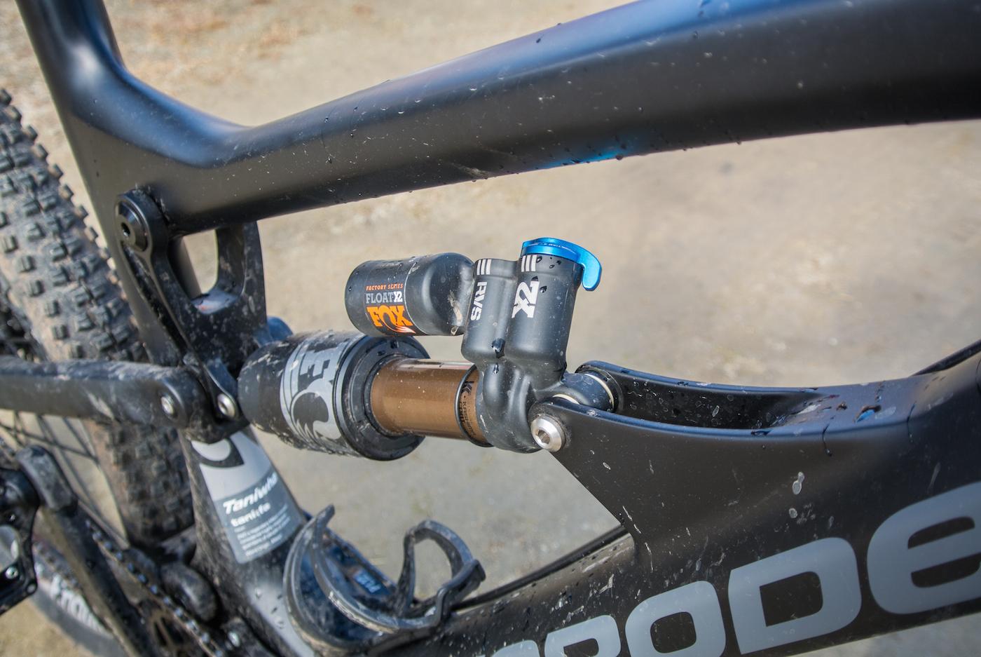 Zerode Taniwha: Close-up view of a mountain bike frame featuring a FOX Float X2 shock absorber mounted on the rear suspension. The frame is partly covered in dirt, indicating recent use. The background shows a blurred, natural surface.