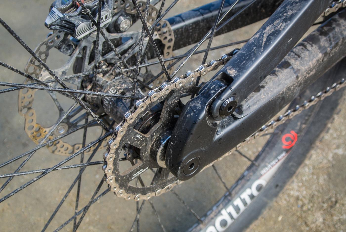 Zerode Taniwha: Close-up view of a mountain bike's rear wheel, featuring a dirty chain, sprocket, and disc brakes, highlighting the intricate details of the bike's drivetrain and wheel components.