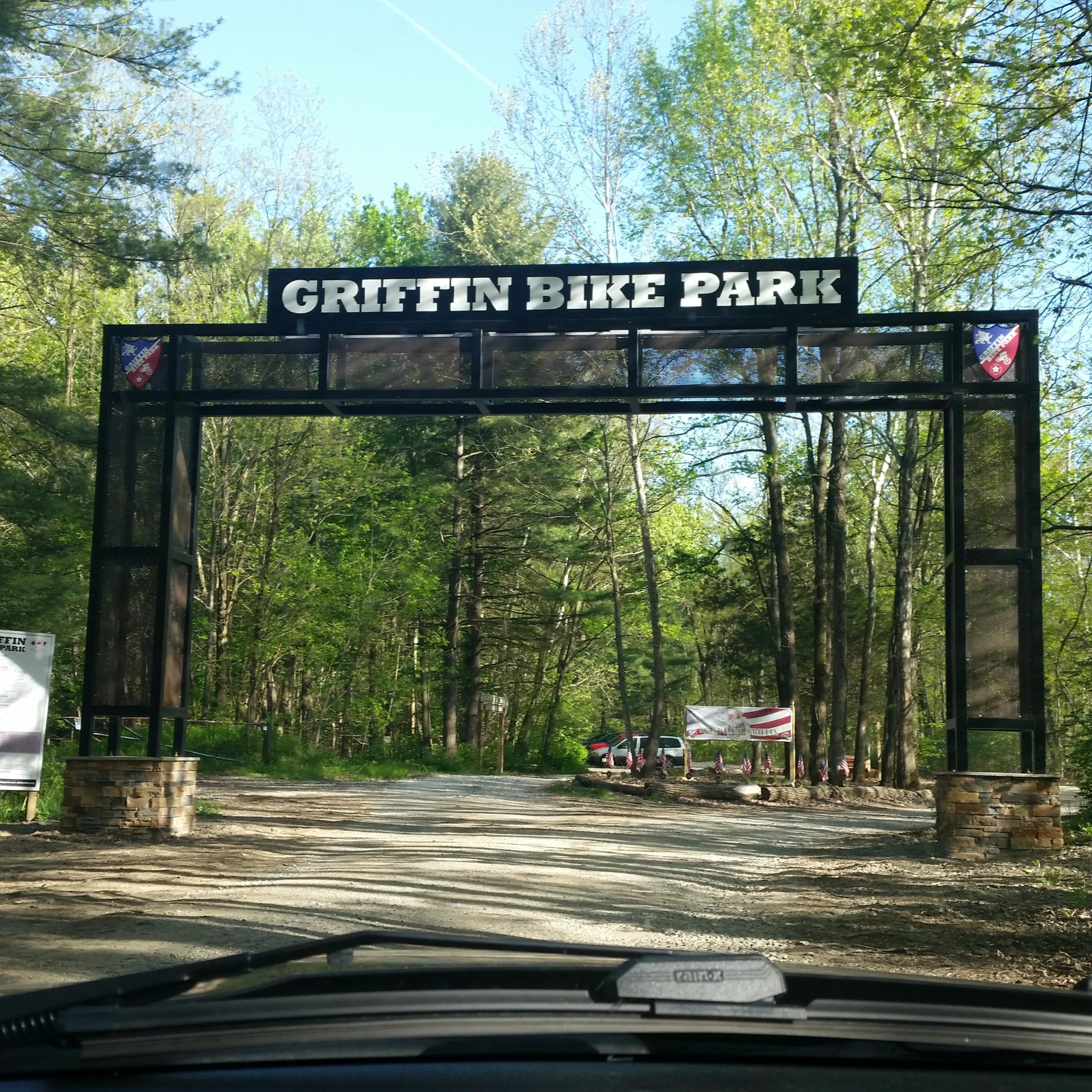 Entrance to Griffin Bike Park, featuring a large archway sign with the park's name, surrounded by lush green trees and a gravel road leading into the park. Griffin Bike Park mountain bike trail.