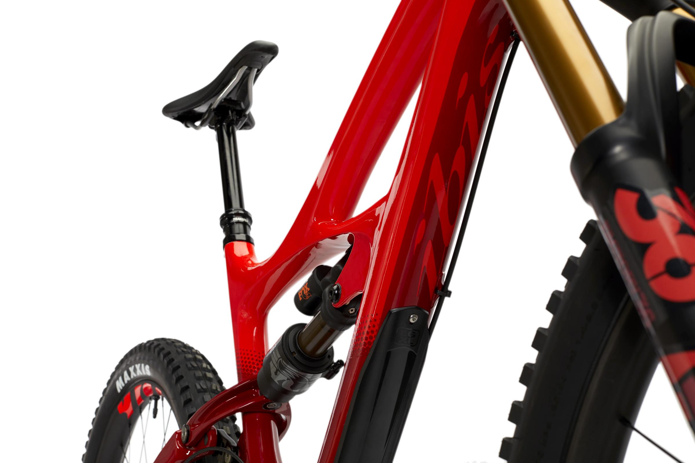 Ibis Mojo HD4: A close-up view of a sleek red mountain bike, highlighting the frame, seat post, and rear shock. The bike features a modern design with high-quality components, including a curved seat and sturdy tires. The background is plain white, emphasizing the bike's vibrant color and intricate details.