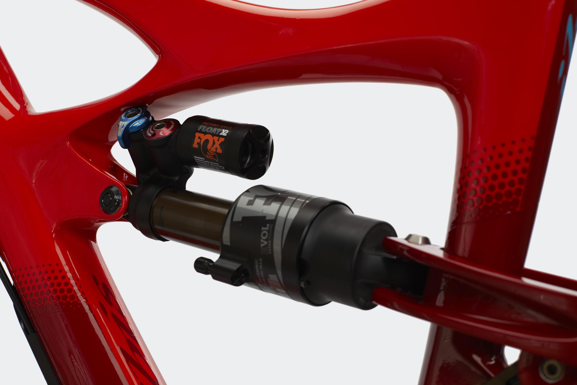 Ibis Mojo HD4: Close-up view of a red bicycle frame featuring a Fox Float X2 shock absorber and adjustment dials, showcasing the intricate design and engineering of modern mountain bike suspension systems.