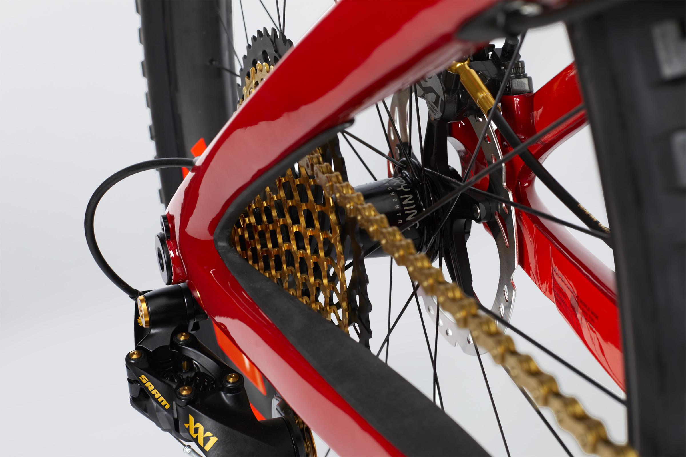 Ibis Mojo HD4: Close-up view of a high-performance mountain bike showcasing the intricate details of the drivetrain, including a shiny gold chain, red frame, and brake components.
