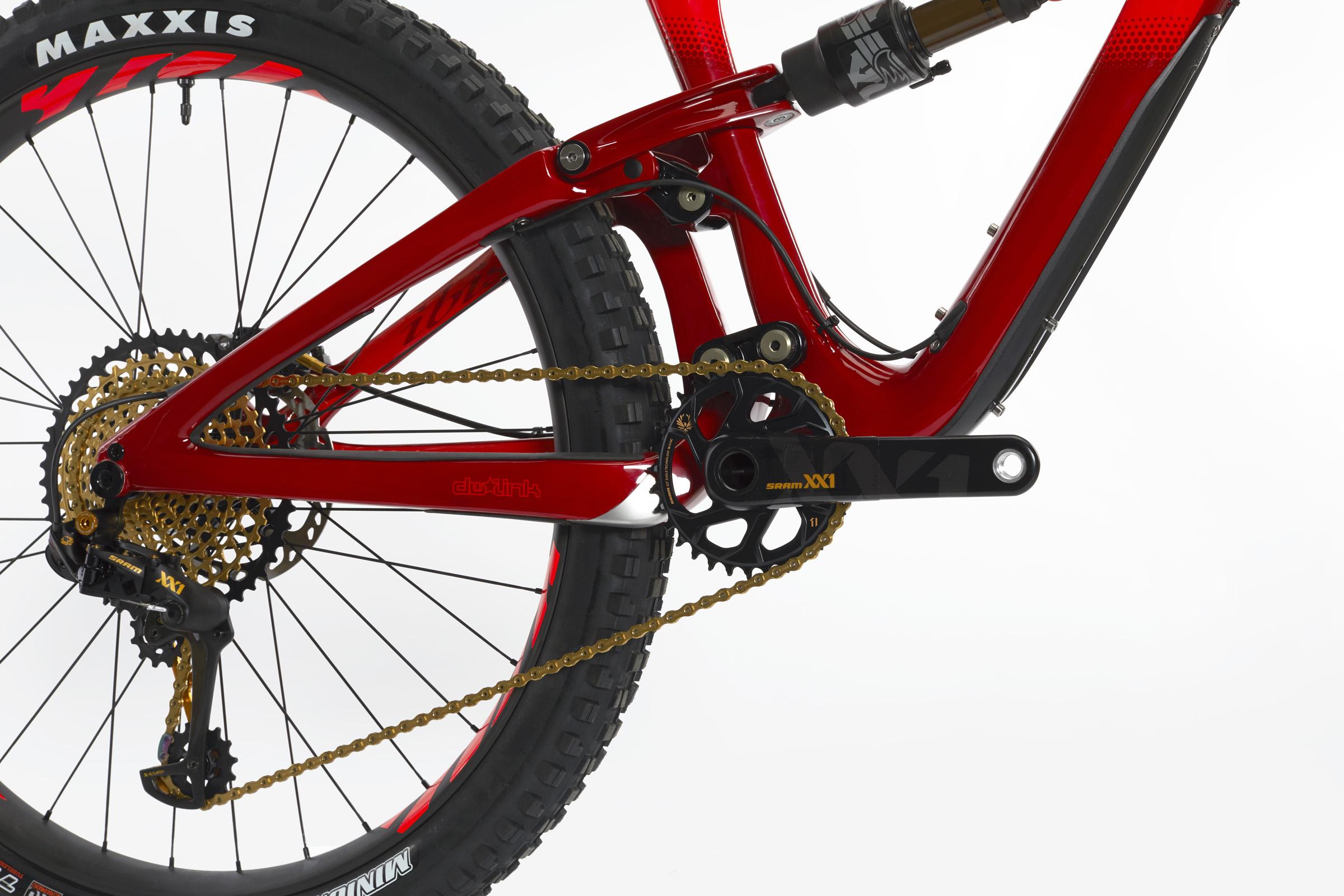 Ibis Mojo HD4: Close-up view of a red mountain bike frame showcasing the crankset and rear derailleur. The bike features a gold chain and is equipped with Maxxis tires, highlighting the intricate details of the drivetrain and suspension components.
