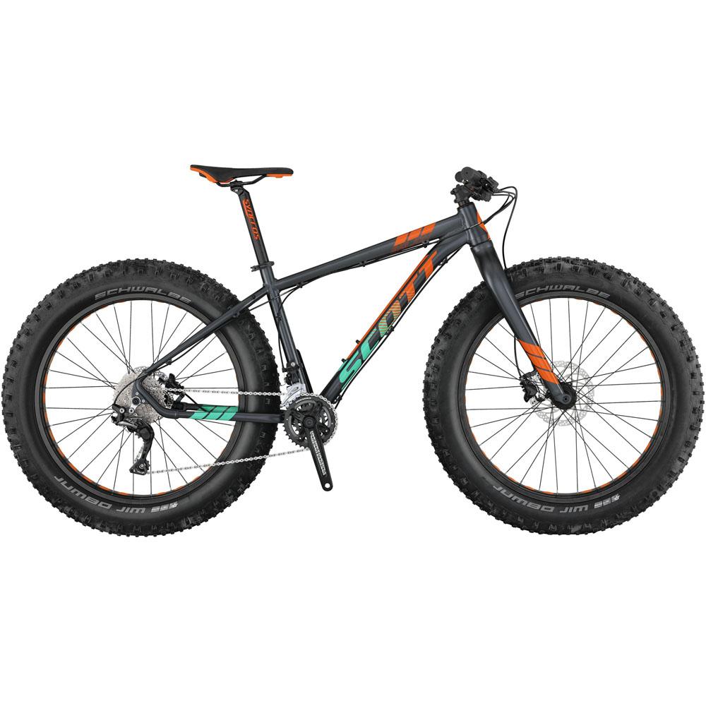Scott Aspect 950: Alt text: A dark gray fat bike with bold orange and green accents, featuring wide tires for improved traction. The bike has a modern design, with a suspension fork, a sleek frame, and a multi-gear setup visible at the rear.