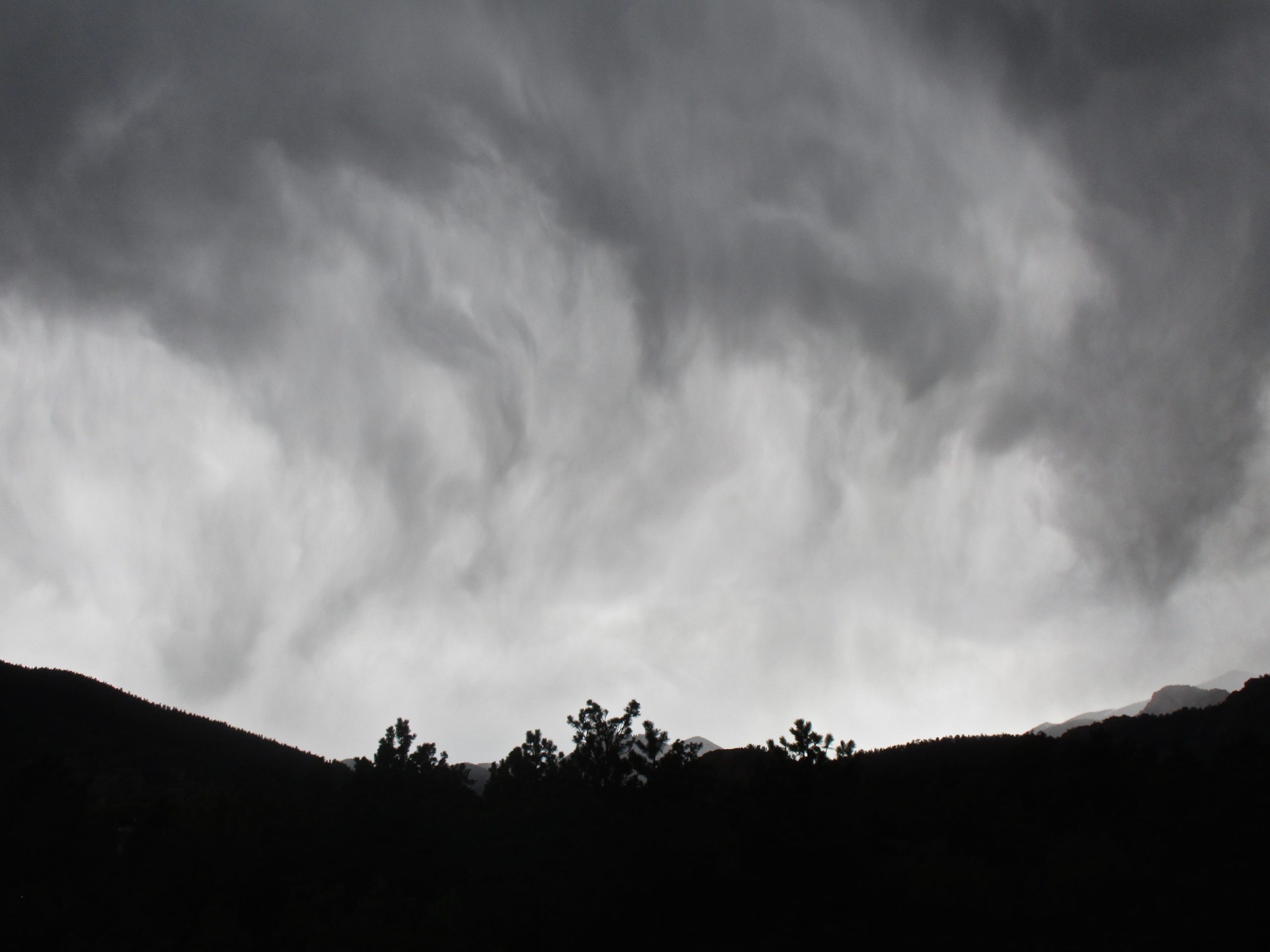 A dramatic sky filled with dark, swirling clouds, contrasted against the silhouette of mountain ridges and trees. The overall atmosphere suggests an impending storm. Stratton Open Space / The Chutes mountain bike trail.