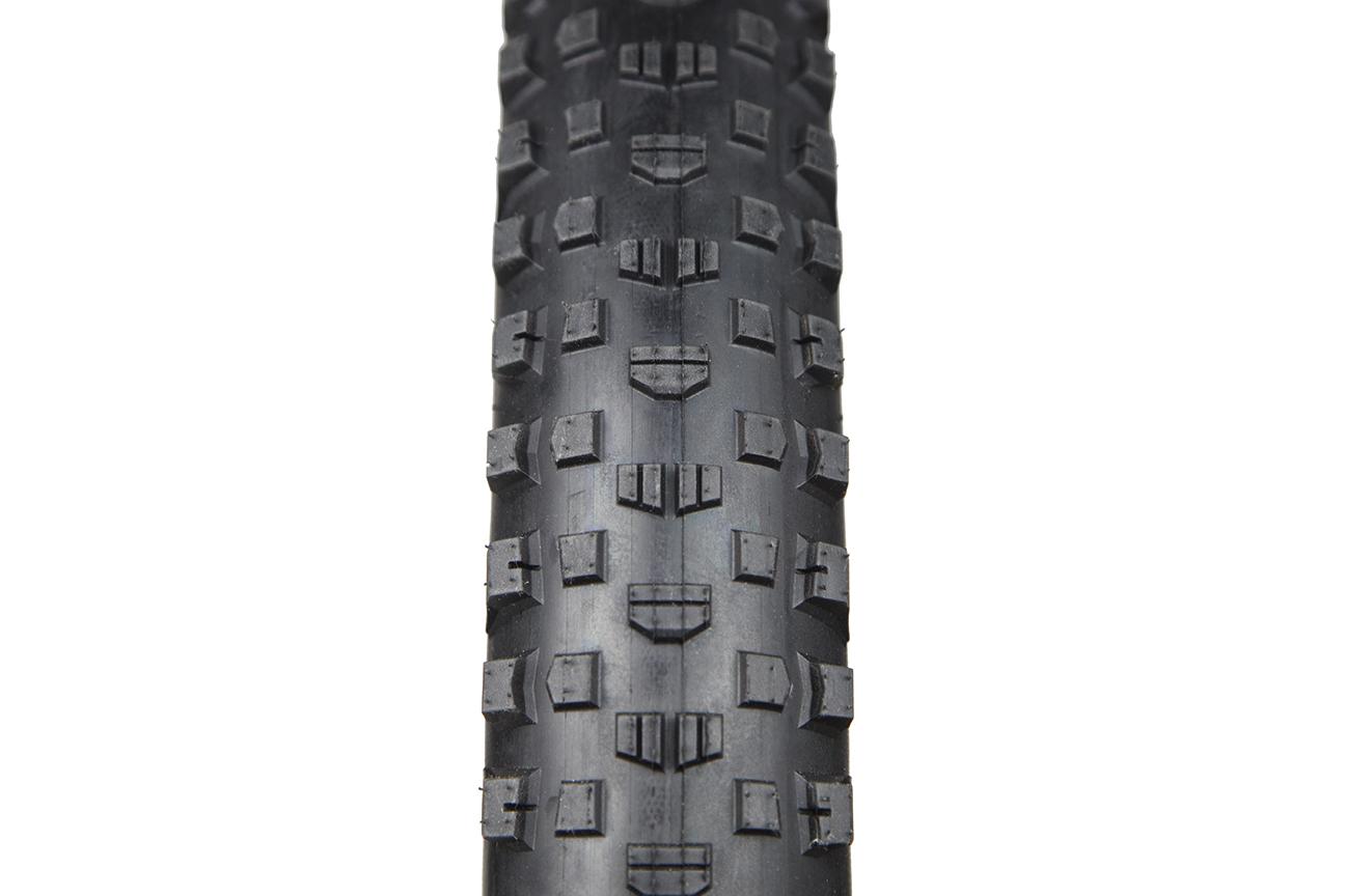 Terrene McFly: Close-up view of a bicycle tire showcasing its tread pattern. The tire features a series of square and rectangular rubber knobs designed for improved traction on various surfaces. The image highlights the texture and depth of the tire, emphasizing its suitability for off-road or rugged terrain.