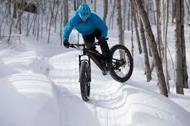 Trek Farley EX8: A person wearing a blue jacket and helmet riding a mountain bike on a snowy trail surrounded by trees, performing a jump over a snowbank.