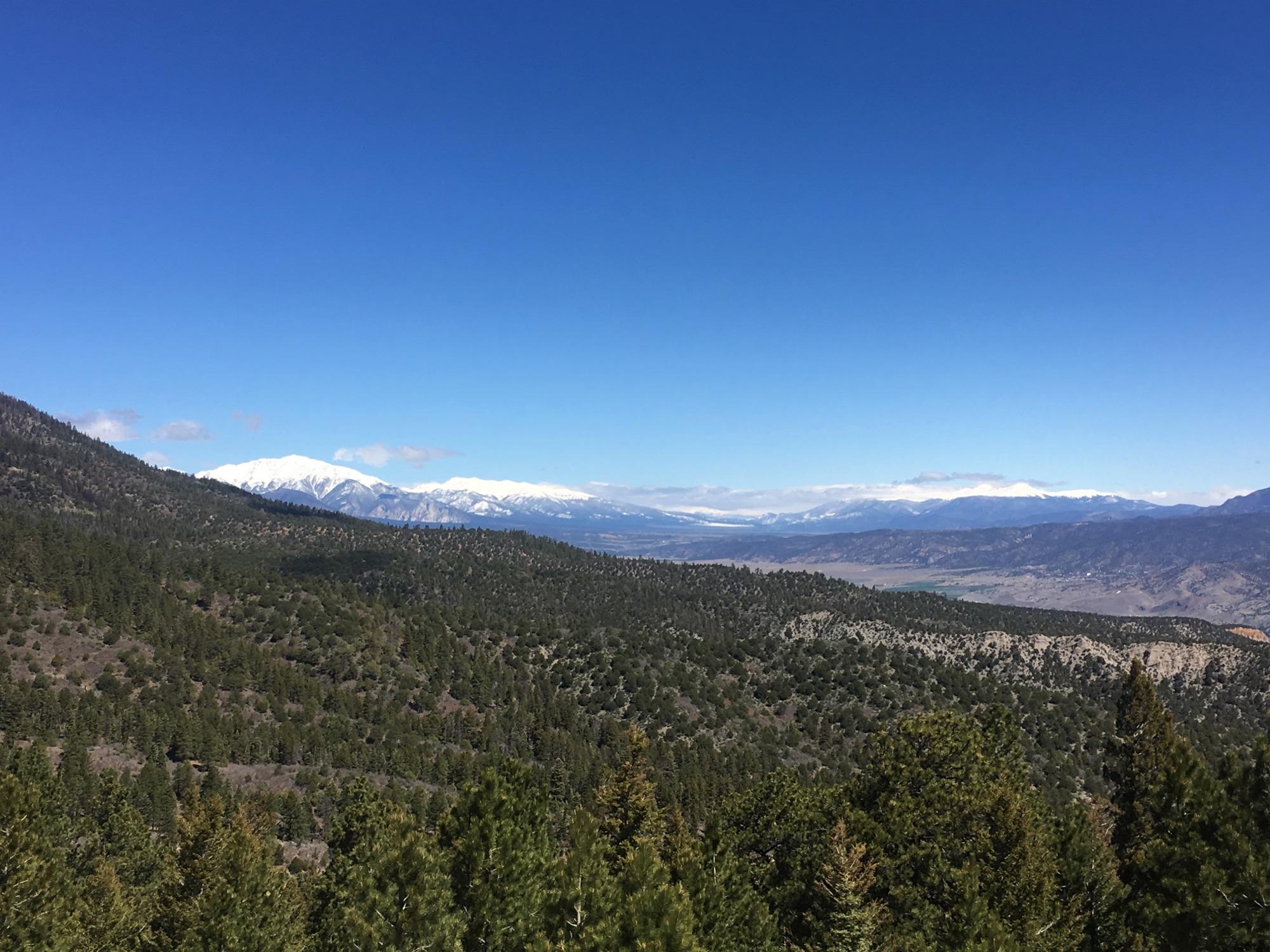 Scenic view of a mountainous landscape featuring snow-capped peaks in the distance, surrounded by dense green forests and a clear blue sky. Rainbow Trail: Methodist Mountain Thd to Bear Creek Thd mountain bike trail.