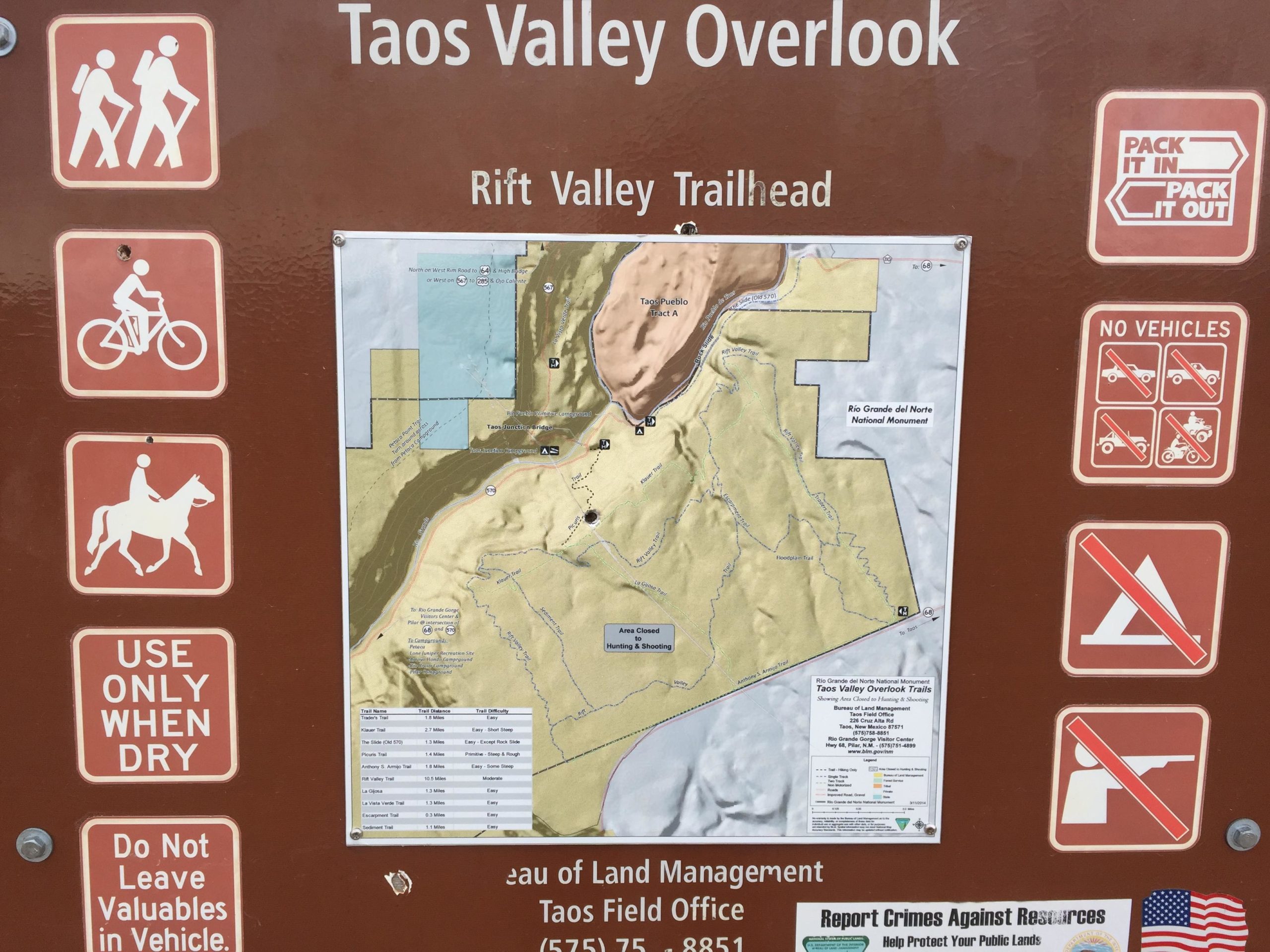 Alt text: "Information sign at Taos Valley Overlook featuring a trail map and icons indicating permitted activities such as hiking, biking, and horseback riding. It includes guidelines for trail use, a reminder to pack in and pack out, and prohibitions on vehicle access, camping, and firearms." Taos Valley Overlook mountain bike trail.