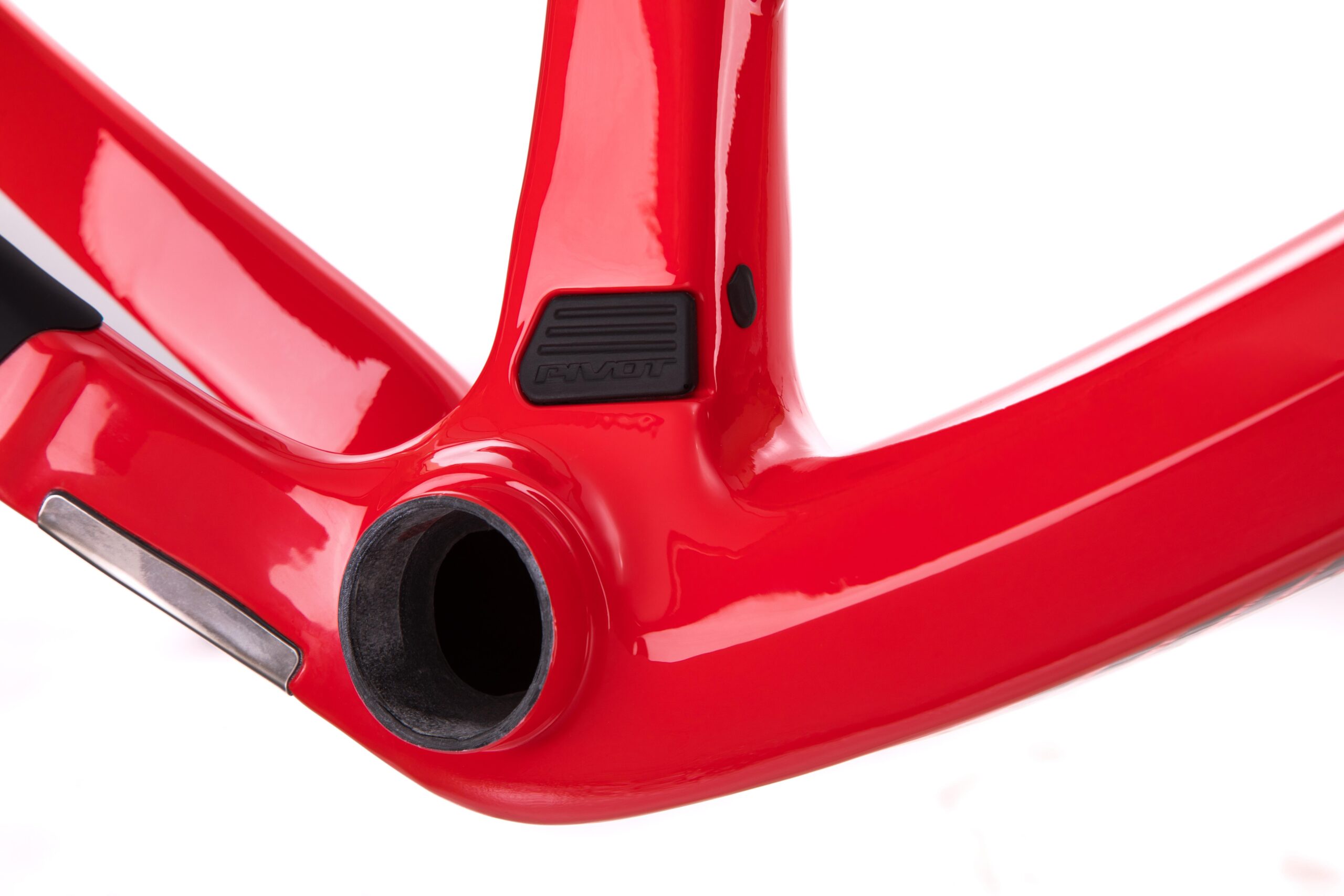 Pivot LES 27.5: Close-up view of a shiny red bicycle frame, highlighting the bottom bracket area with a pivot logo, showcasing smooth curves and a sleek design. The background is white, emphasizing the vibrant color and details of the frame.