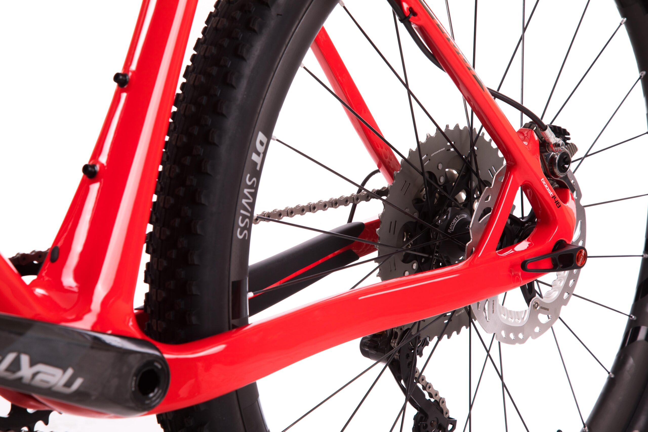 Pivot LES 27.5: A close-up view of a mountain bike's rear frame, showcasing the vibrant red paint, chainstay, and derailleur. The image highlights the bike's disc brake system and the textured tire, with visible details of the chain and gears. The background is plain white, emphasizing the bicycle components.