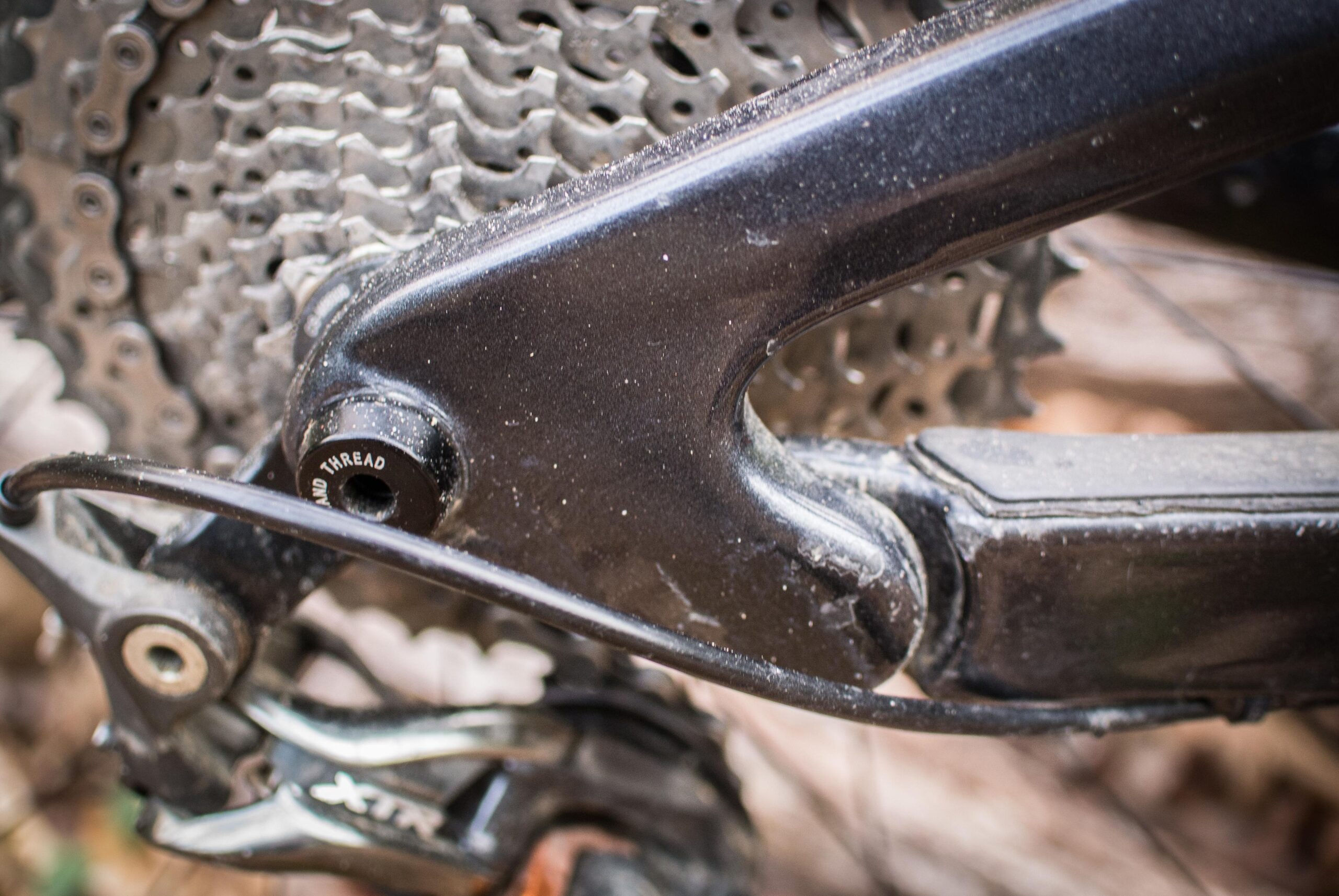 Rocky Mountain Element: Close-up of a mountain bike's rear derailleur and cassette, showcasing the detailed components including the chain, gear teeth, and housing elements. The parts are slightly dusty, indicating recent use on rugged terrain.