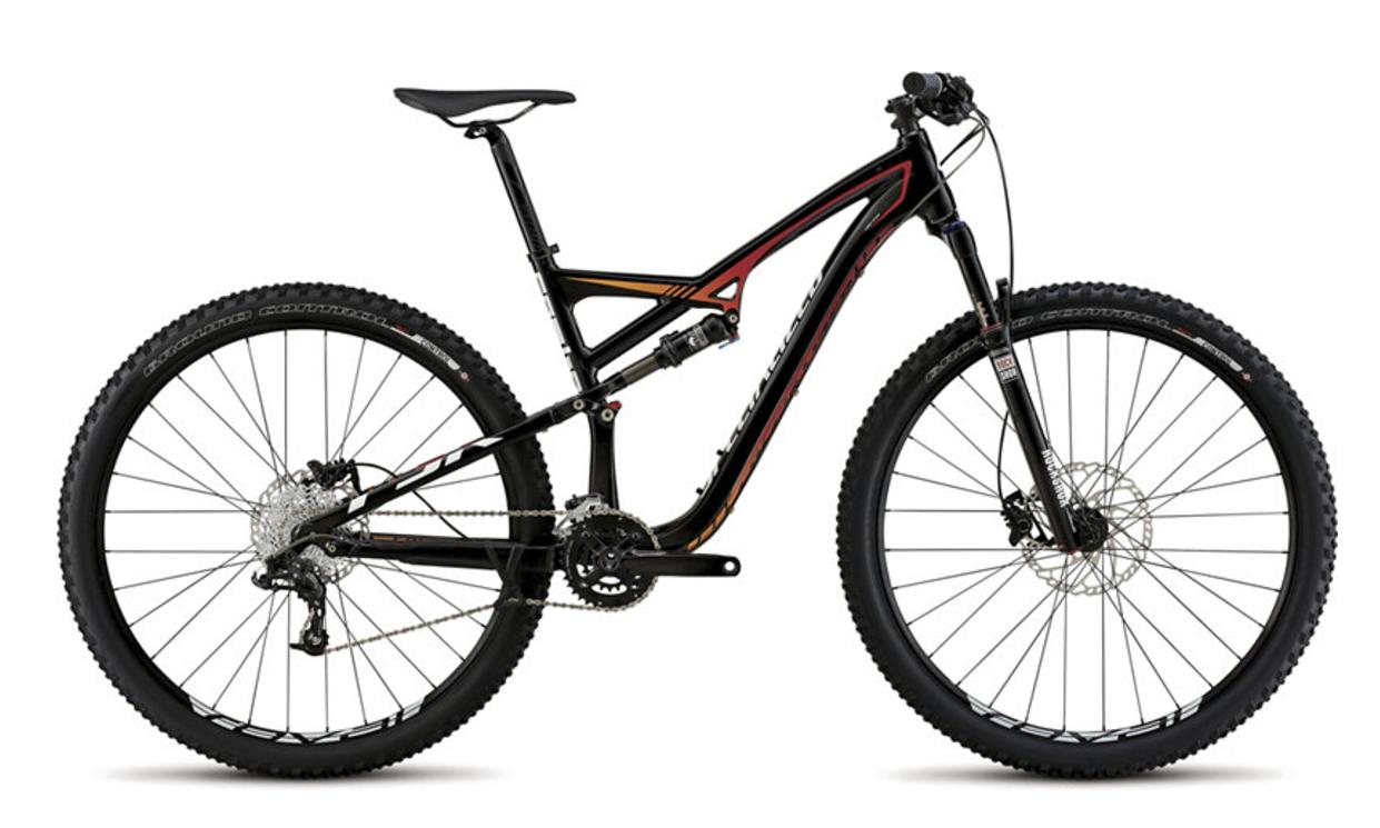 Specialized Camber Comp 29: Alt text: A black and orange mountain bike seen from the side, featuring thick tires, a dual suspension system, and disc brakes. The bike has a sleek design with a lightweight frame and gear system.