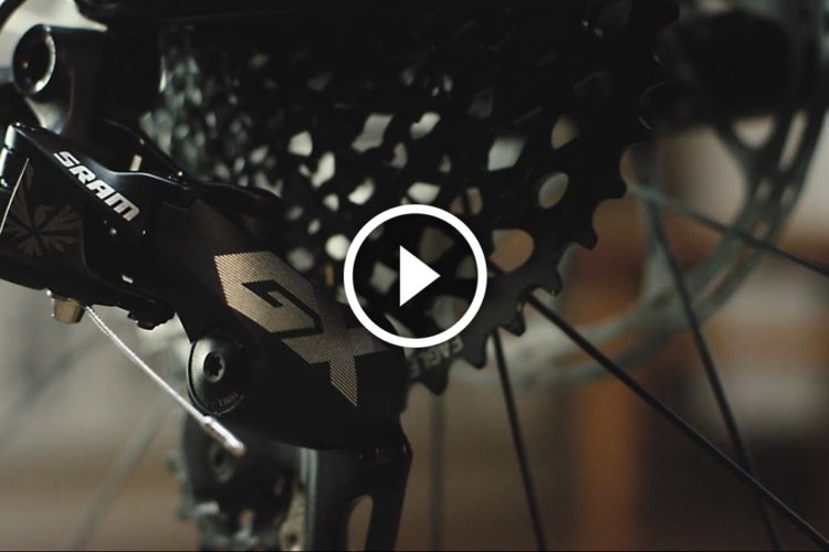 Close-up view of a SRAM GX bike derailleur mounted on a bicycle, with sunlight highlighting the intricate details of the component and the surrounding gears.