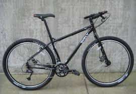 Surly Ogre: A black mountain bike with a sturdy frame, wide tires, and a single suspension fork, positioned against a concrete wall.