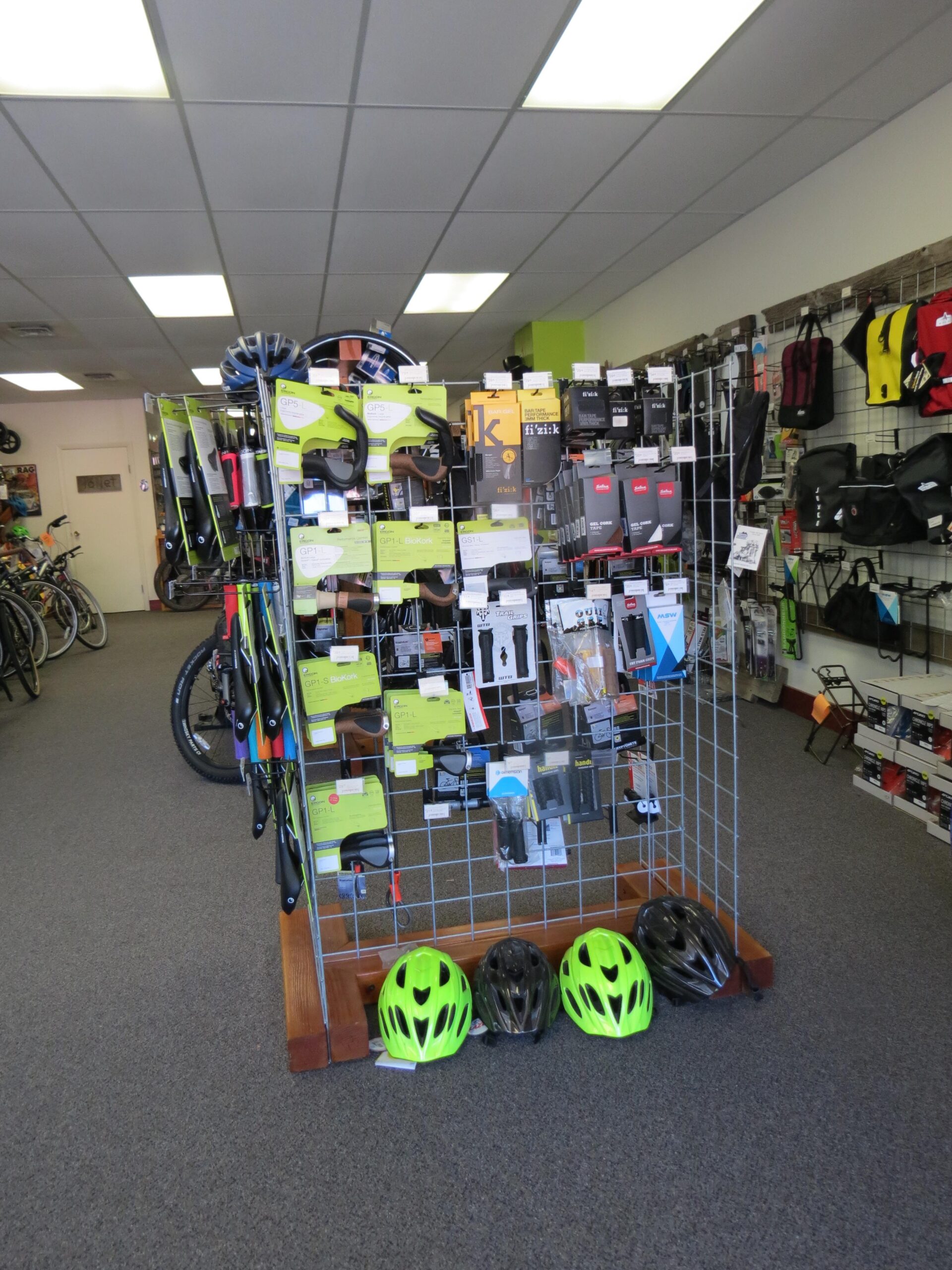 Image alt tag: A display rack inside a bike shop featuring various cycling accessories and equipment, with several bicycle helmets displayed at the bottom. The shop has a bright, organized layout, showcasing items like GPS devices and bike parts.