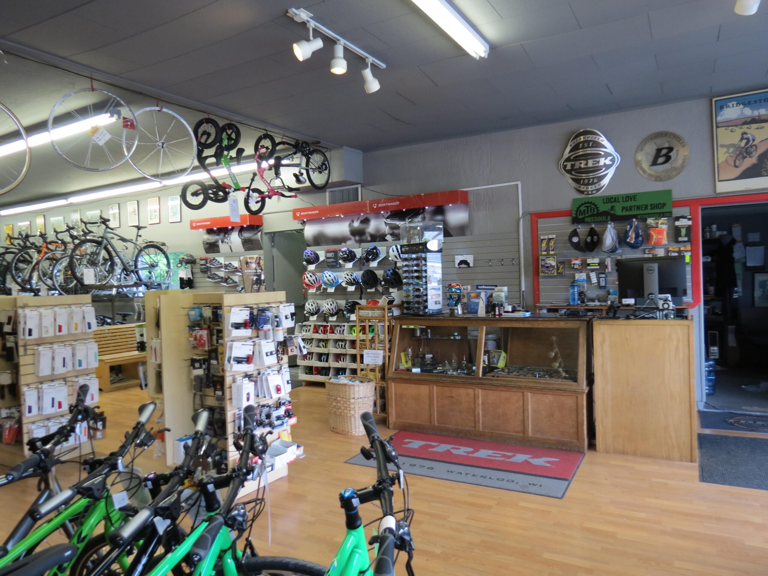 Alt text: Interior of a bicycle shop featuring various bicycles on display, shelves stocked with accessories, and a sales counter with a wooden display case. The shop has a clean and organized layout with bright lighting.