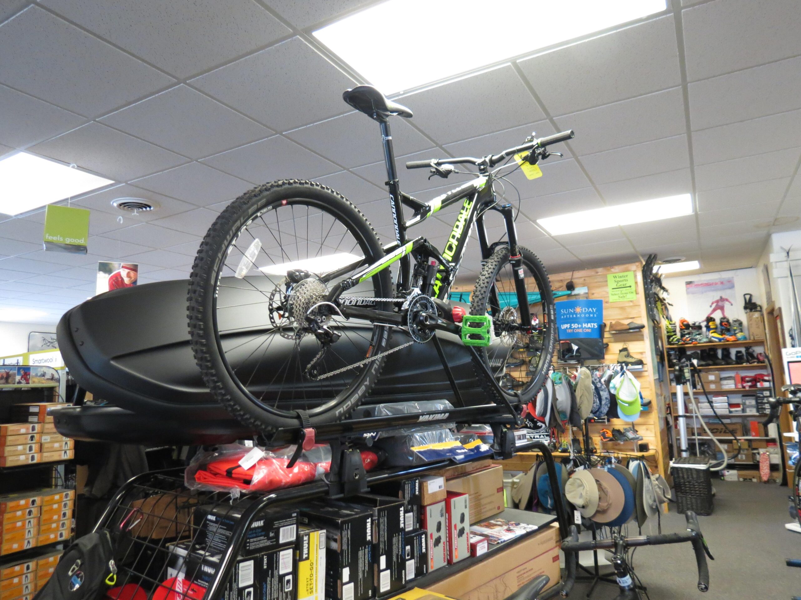 A mountain bike displayed on top of storage boxes inside a sporting goods store, with shelves filled with outdoor gear and accessories in the background.