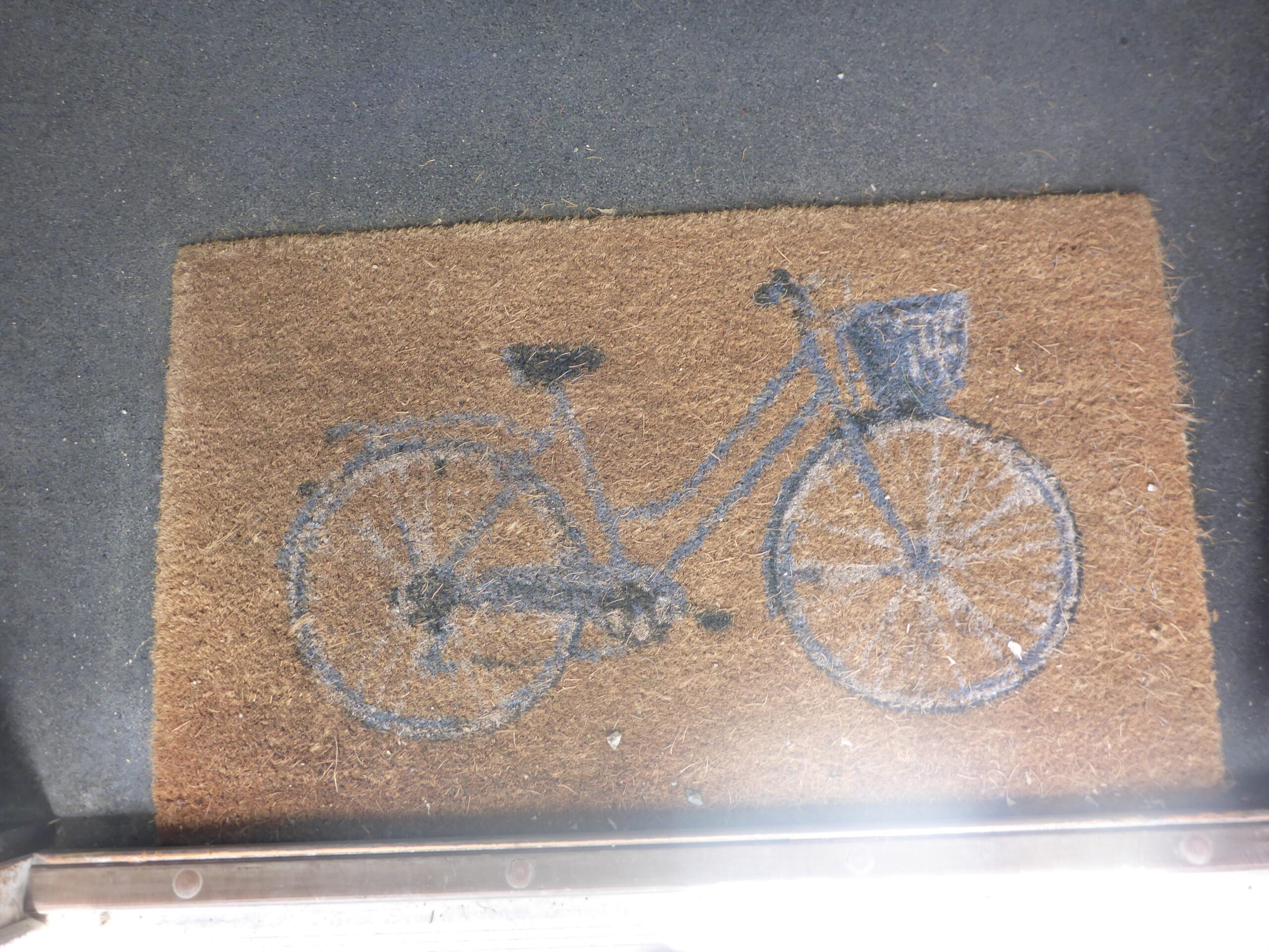 Coir doormat featuring a blue illustration of a bicycle on a brown background.
