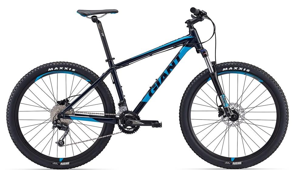 Giant Talon 27.5 2: Alt text: A blue and black mountain bike with the brand name "Giant" prominently displayed on the frame. The bike features wide tires branded with "Maxxis" and is shown from the side, highlighting its sturdy construction and gear system.