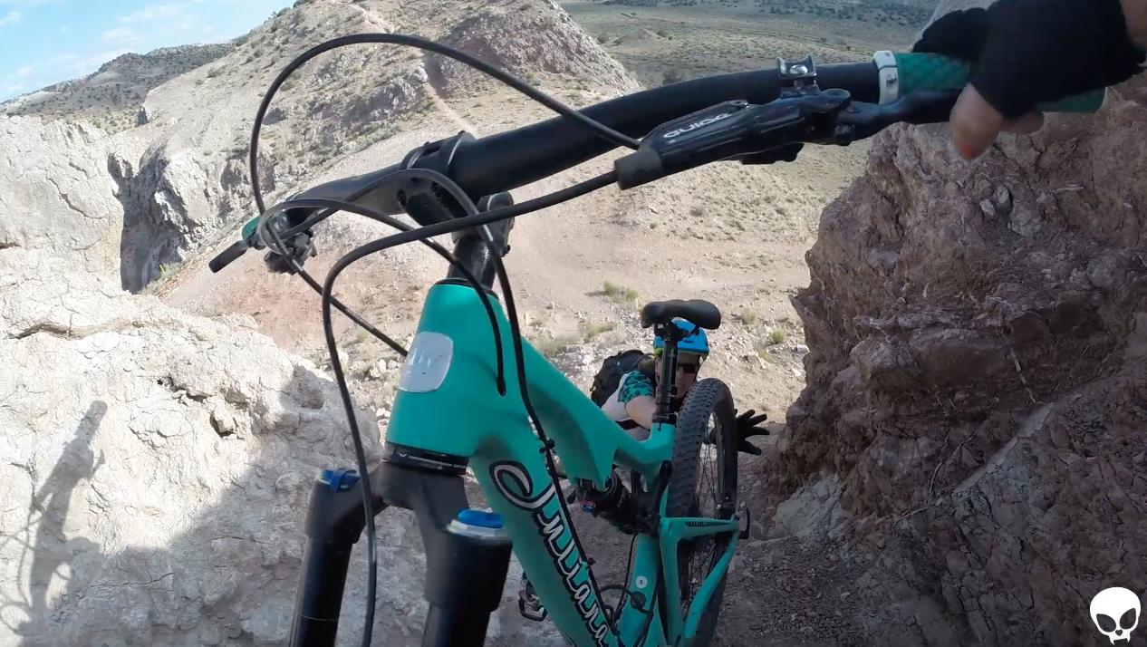 A mountain biker navigating a rocky terrain, with a view of steep slopes and rugged landscape in the background. The bike is positioned prominently in the foreground, showcasing its frame and handlebars, while the rider is partially visible as they maneuver over the rocky surface. White Ridge Bike Trails mountain bike trail.