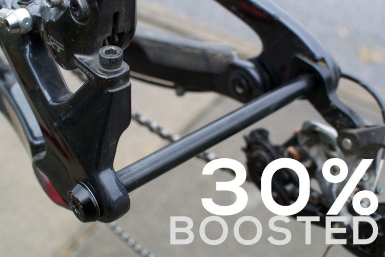 Close-up image of a bicycle's rear drivetrain component, showcasing the linkage and details of the black frame. Overlaid text reads "30% BOOSTED."