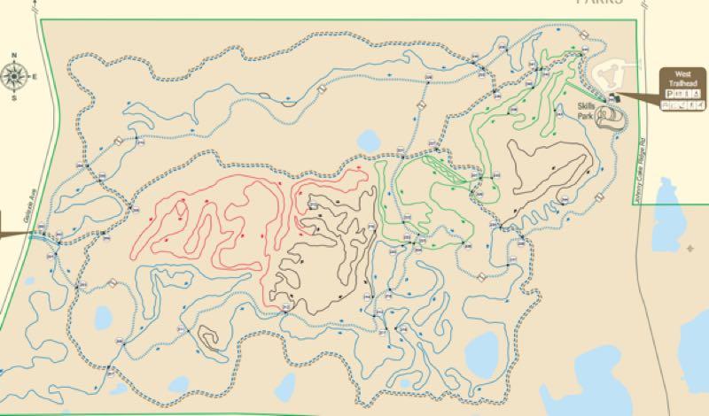 Map of a park trail system, featuring winding paths marked in various colors (red, black, green, and blue) to indicate different trails. The map includes a compass rose, key locations such as a skills park, and highlights water bodies. Lebanon Hills mountain bike trail.