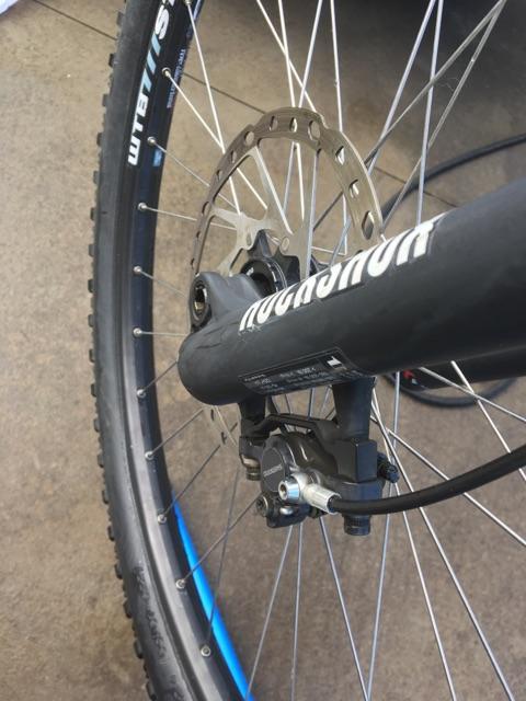 Kona Process 111: Close-up view of a bicycle's disc brake system, featuring the rotor and caliper. The image also shows part of the bike's front tire and fork, with a focus on the brake components.